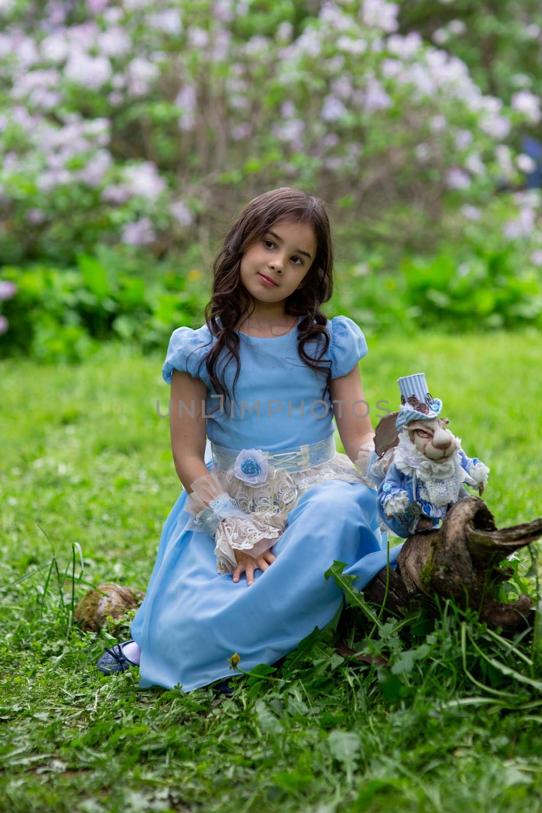 Young brunette girl in blue dress with doll in garden setting.