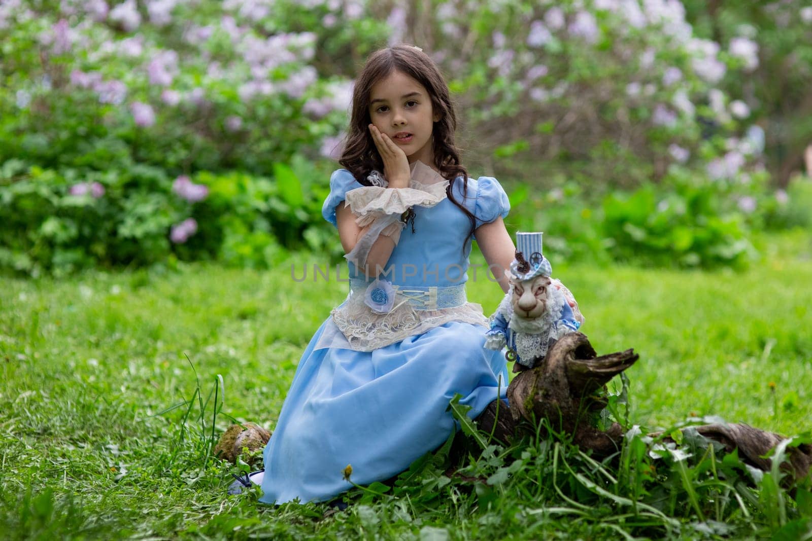 Young pretty girl in blue dress with rabbit toy posing in lush green park.