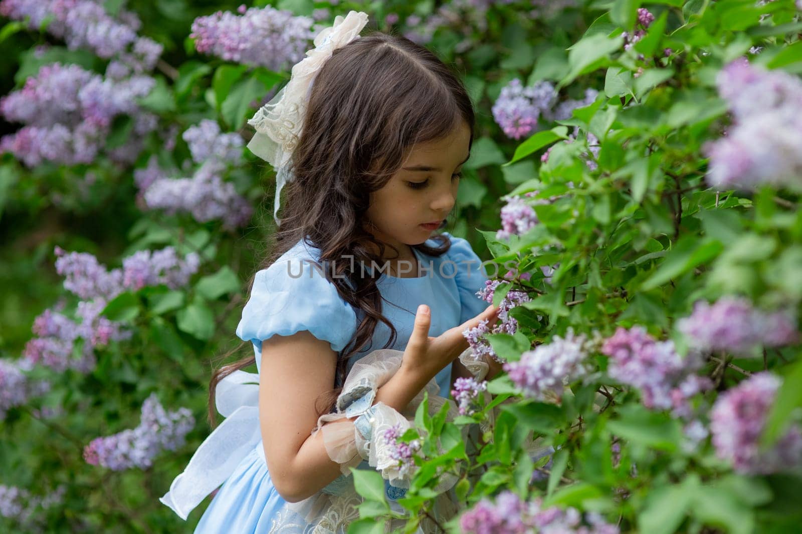 Young caucasian girl admiring lilac flowers in blooming garden.