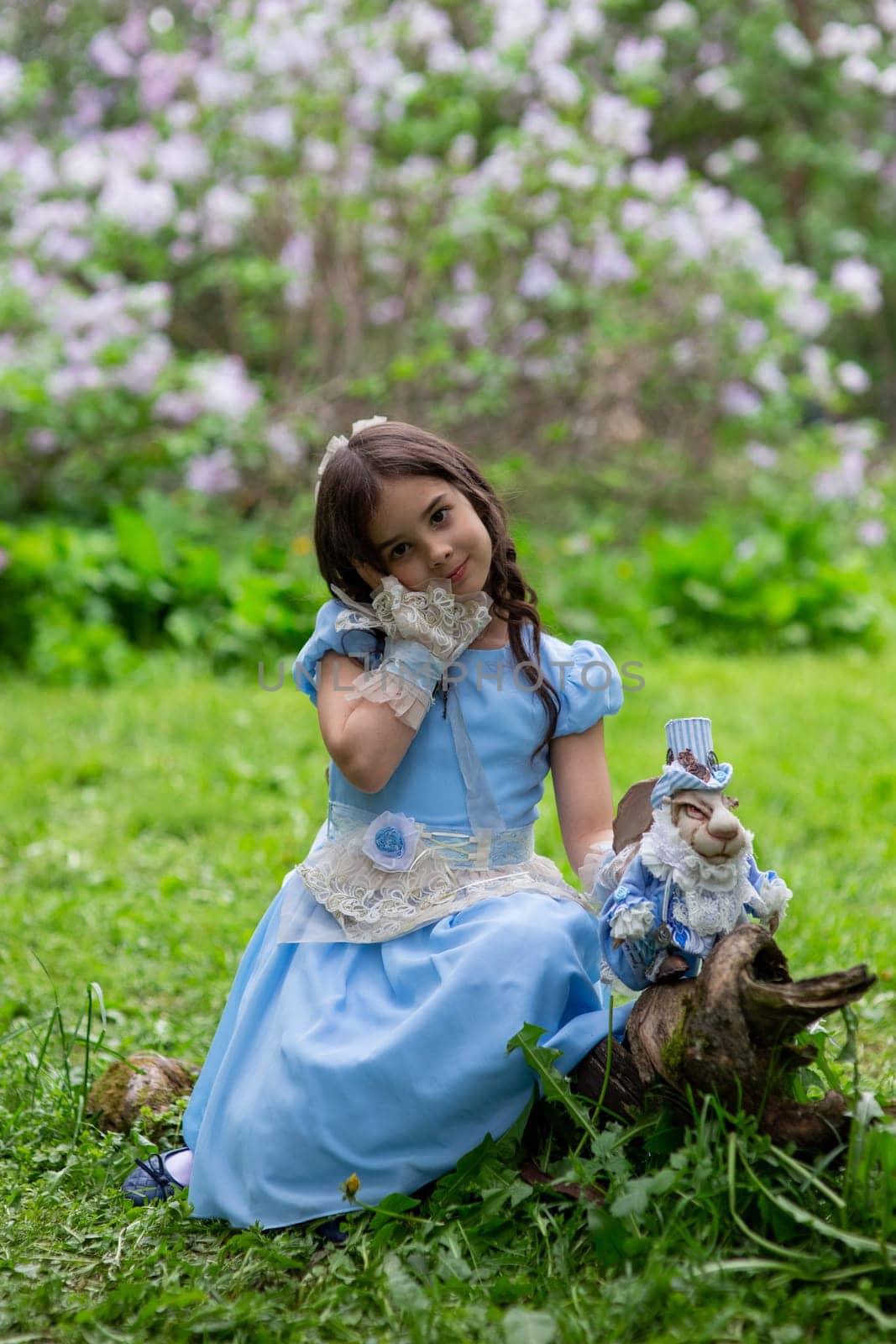 Caucasian female child in blue dress with rabbit doll in garden setting.