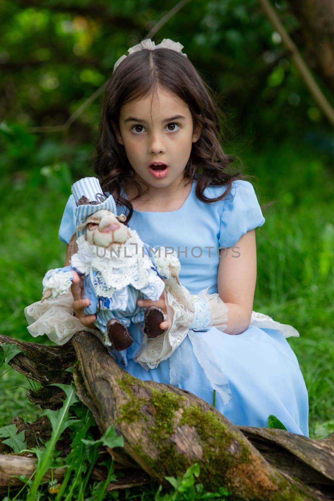 Surprised caucasian female child in blue dress holding rabbit toy in outdoor setting