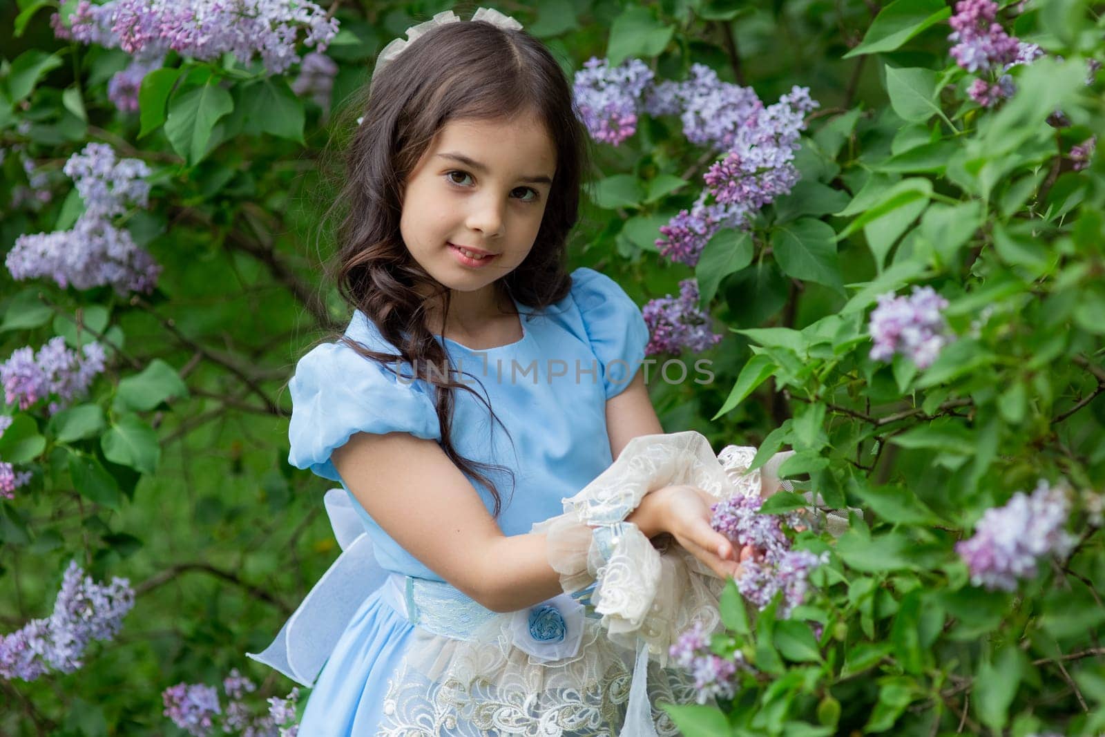 Young caucasian girl in blue dress amidst blooming lilacs.