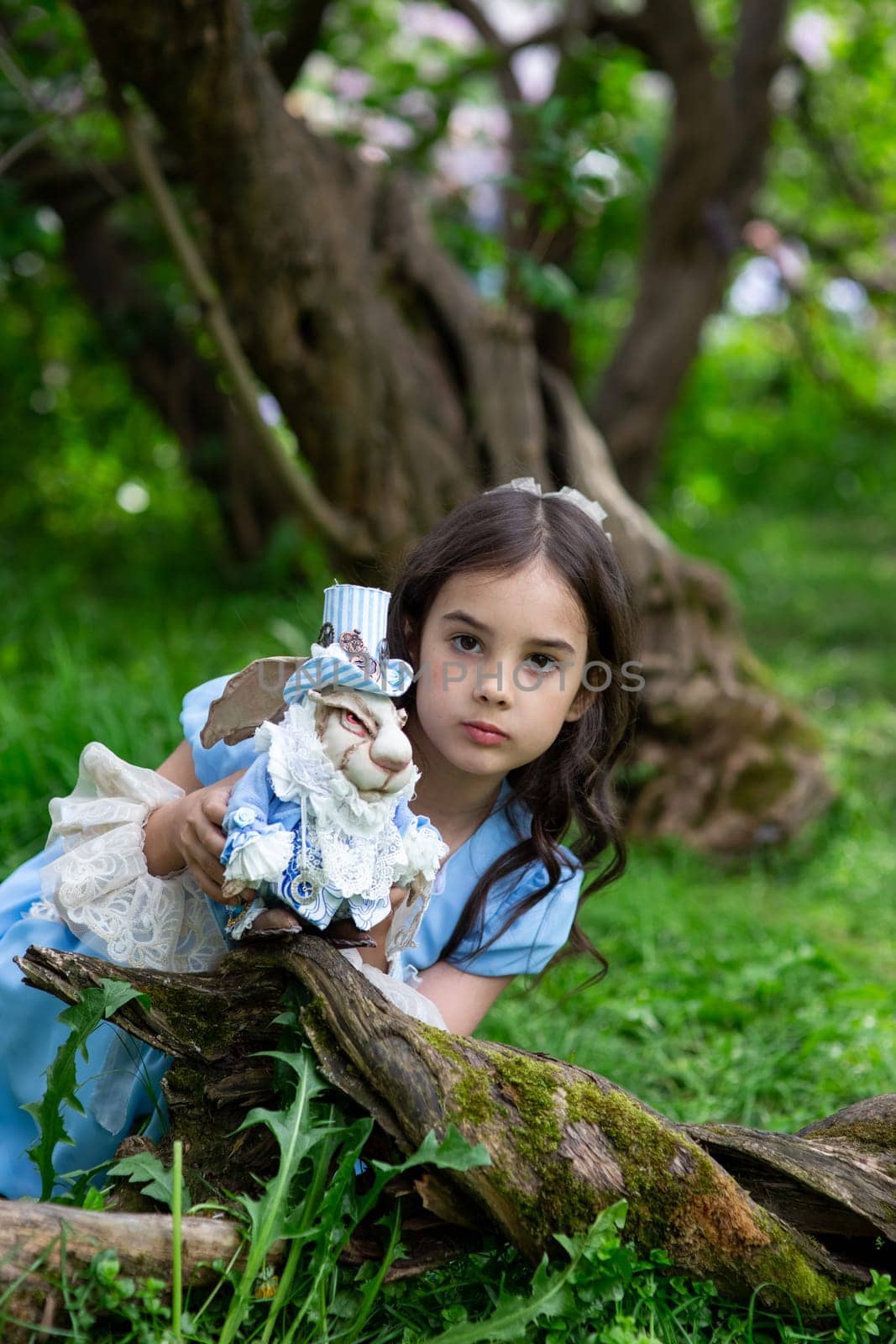 Young caucasian girl in blue dress holding rabbit toy in woodland setting