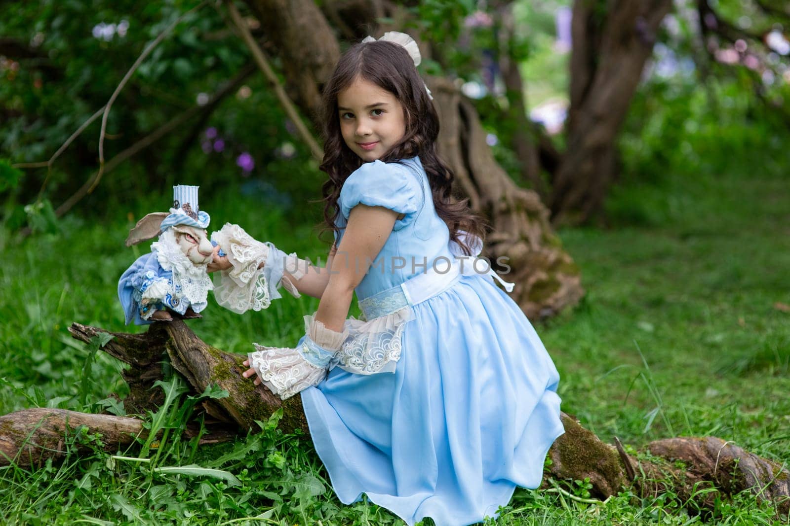 Young caucasian girl in blue dress playing in forest with toy rabbit.