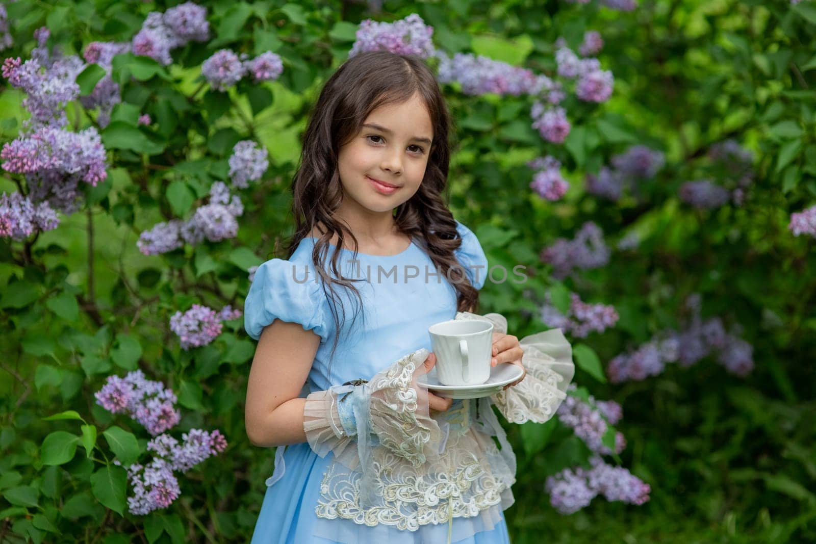 Young caucasian girl in blue dress holding teacup in garden.
