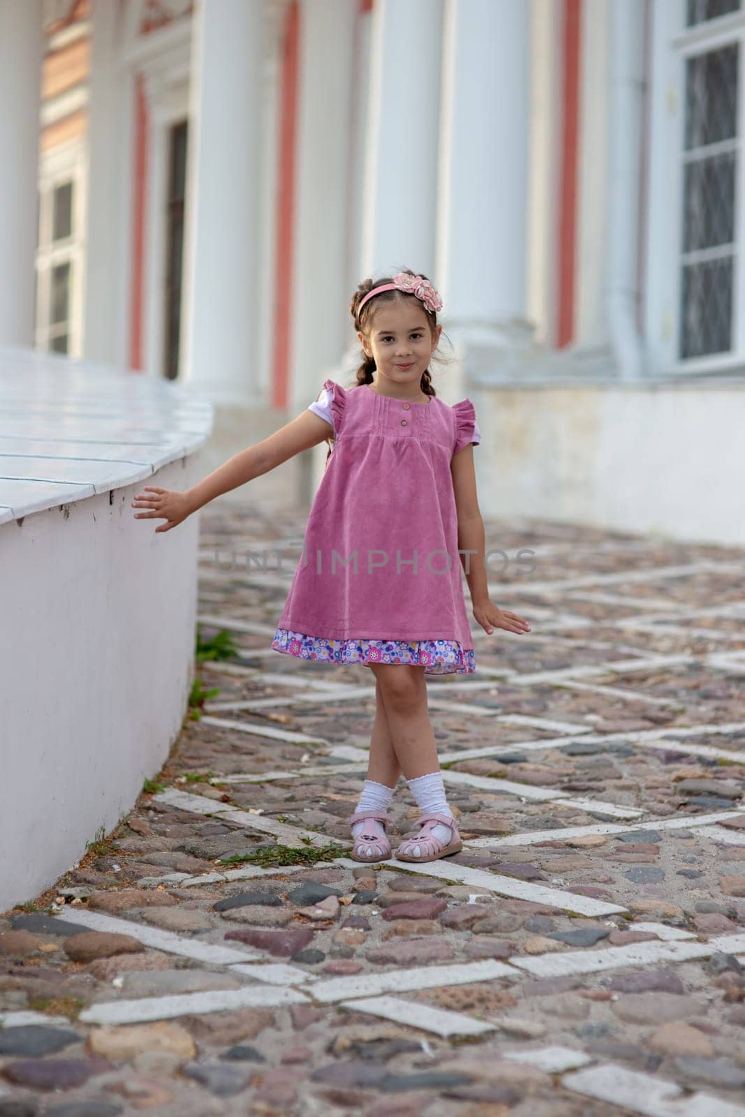 Young caucasian girl in pink dress posing outdoors on cobblestone path.