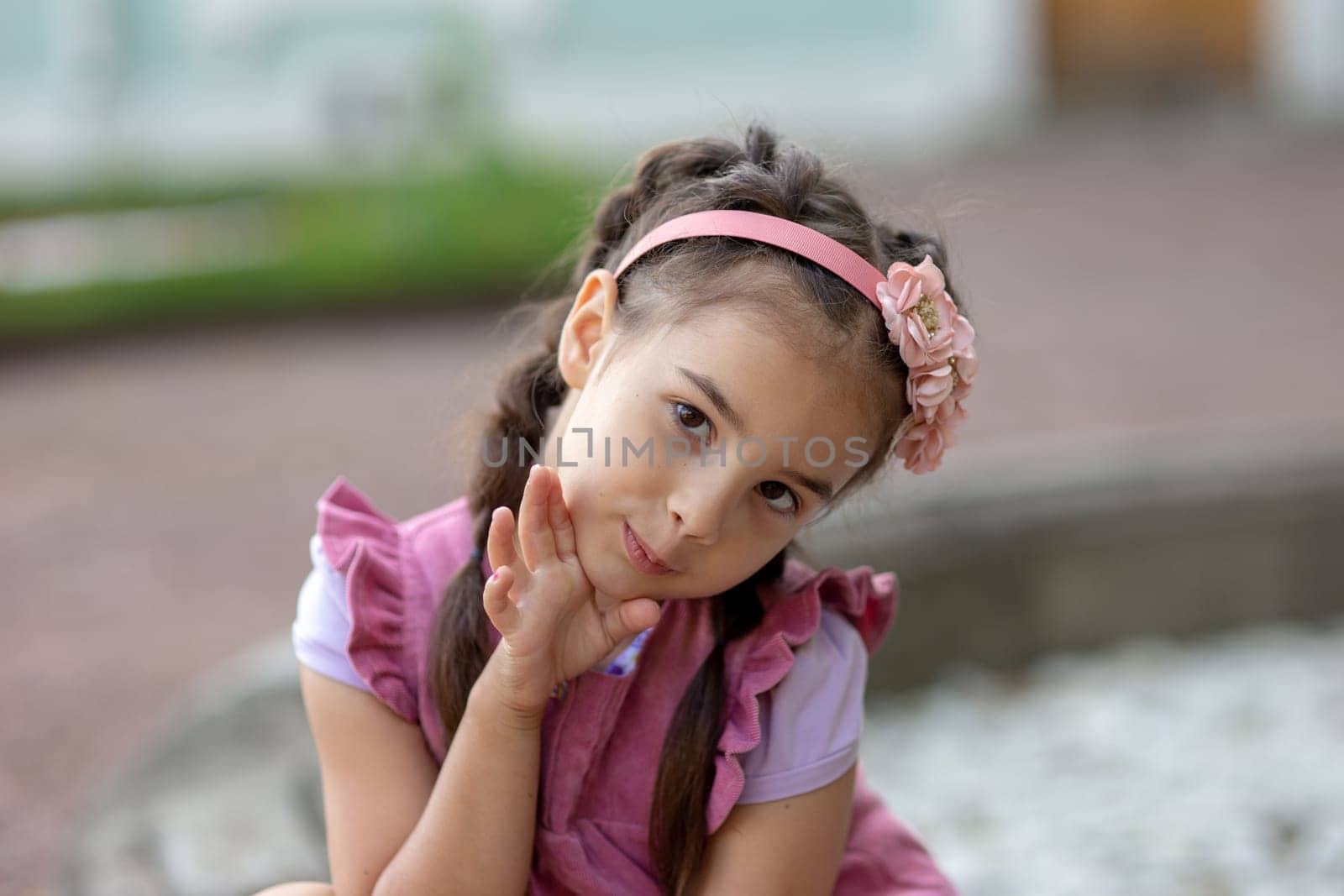 Young caucasian female child in pink dress with flower headband smiling playfully outdoors.