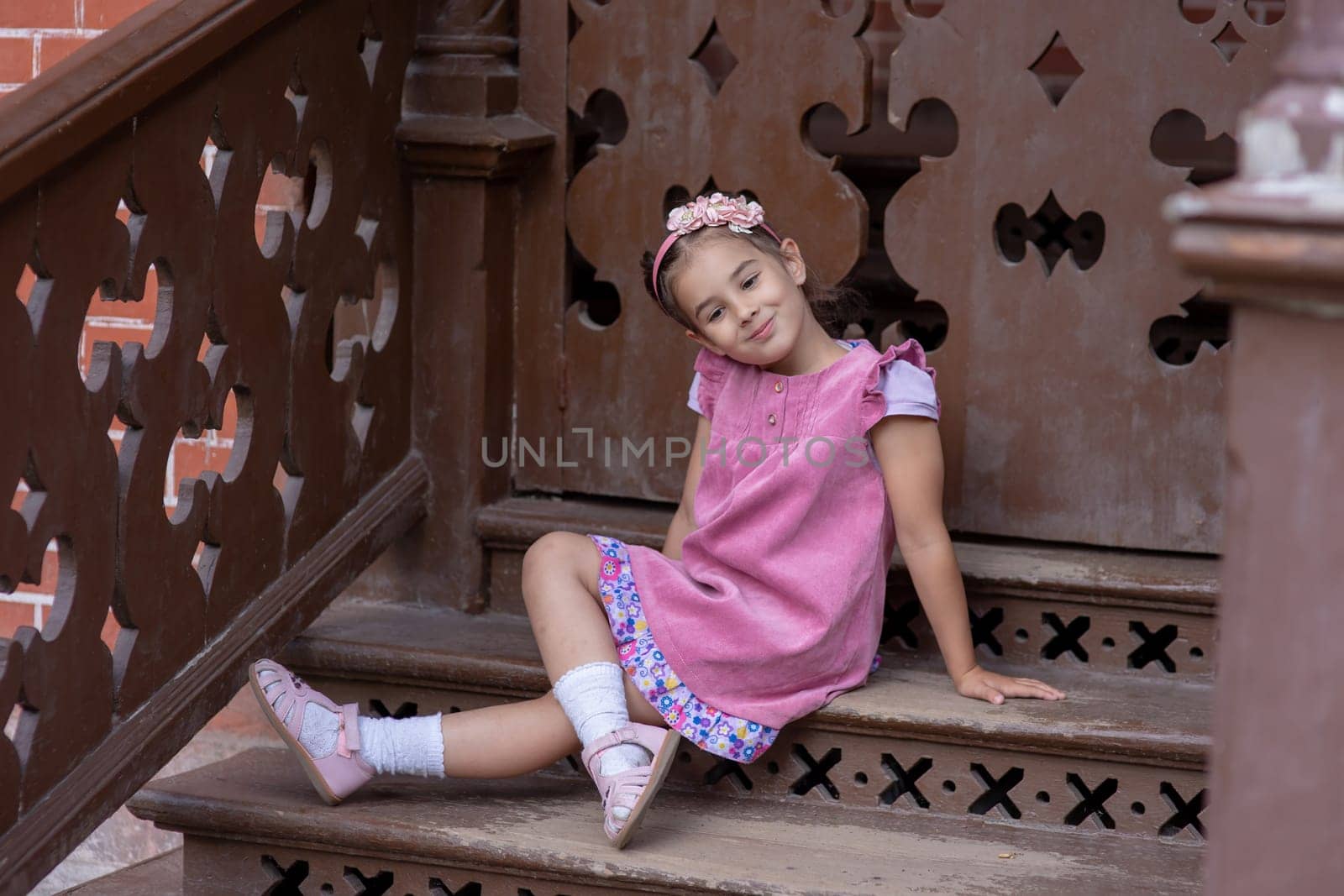 Little girl in pink dress sitting on wooden steps.