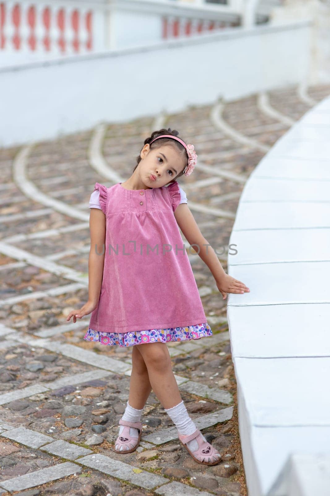 Young caucasian female child in pink dress standing on steps outdoors.
