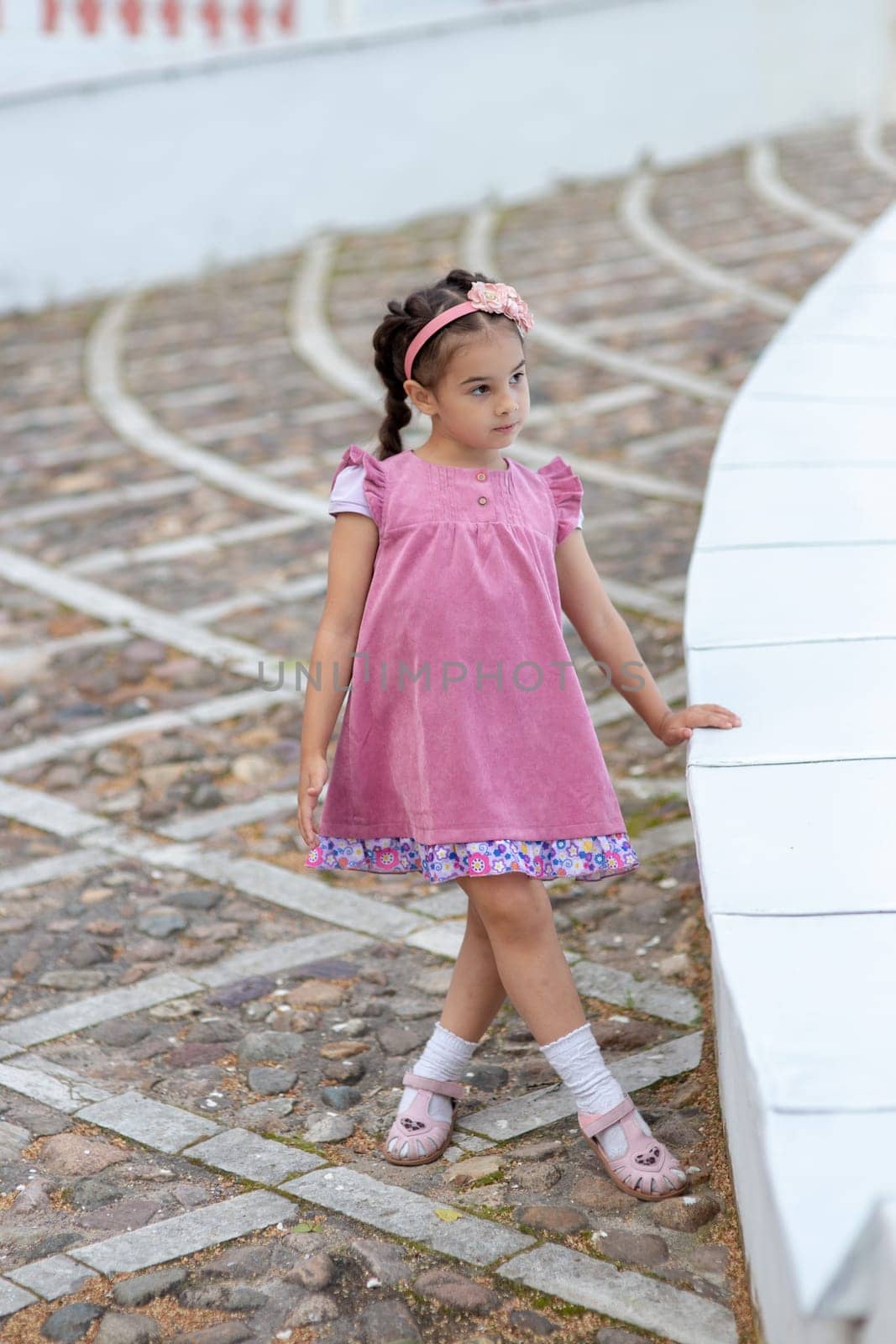 Caucasian young girl in pink dress standing outdoors.