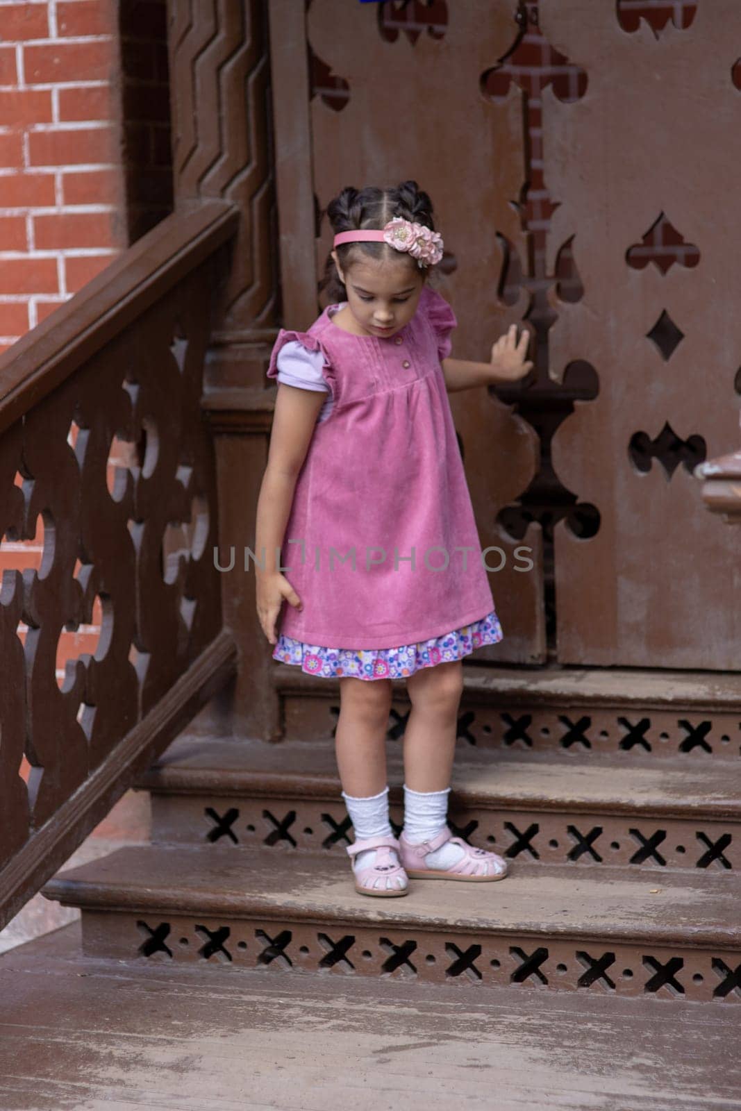 Young caucasian girl in pink dress descending wooden staircase.