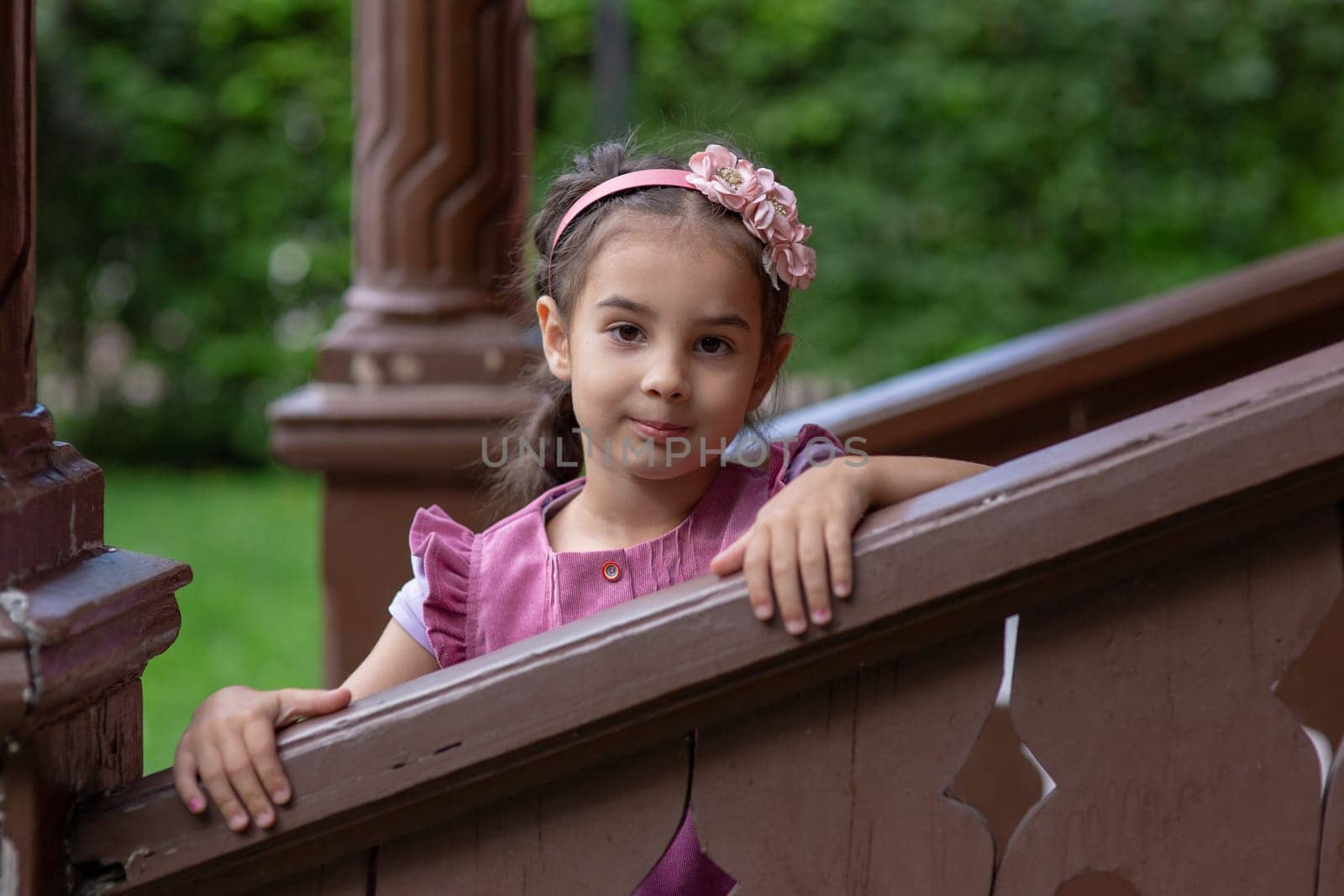 Young caucasian girl with pink headband posing on wooden staircase outdoors.