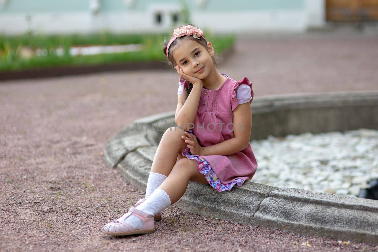 Asian female child in pink dress sitting by a fountain in garden.