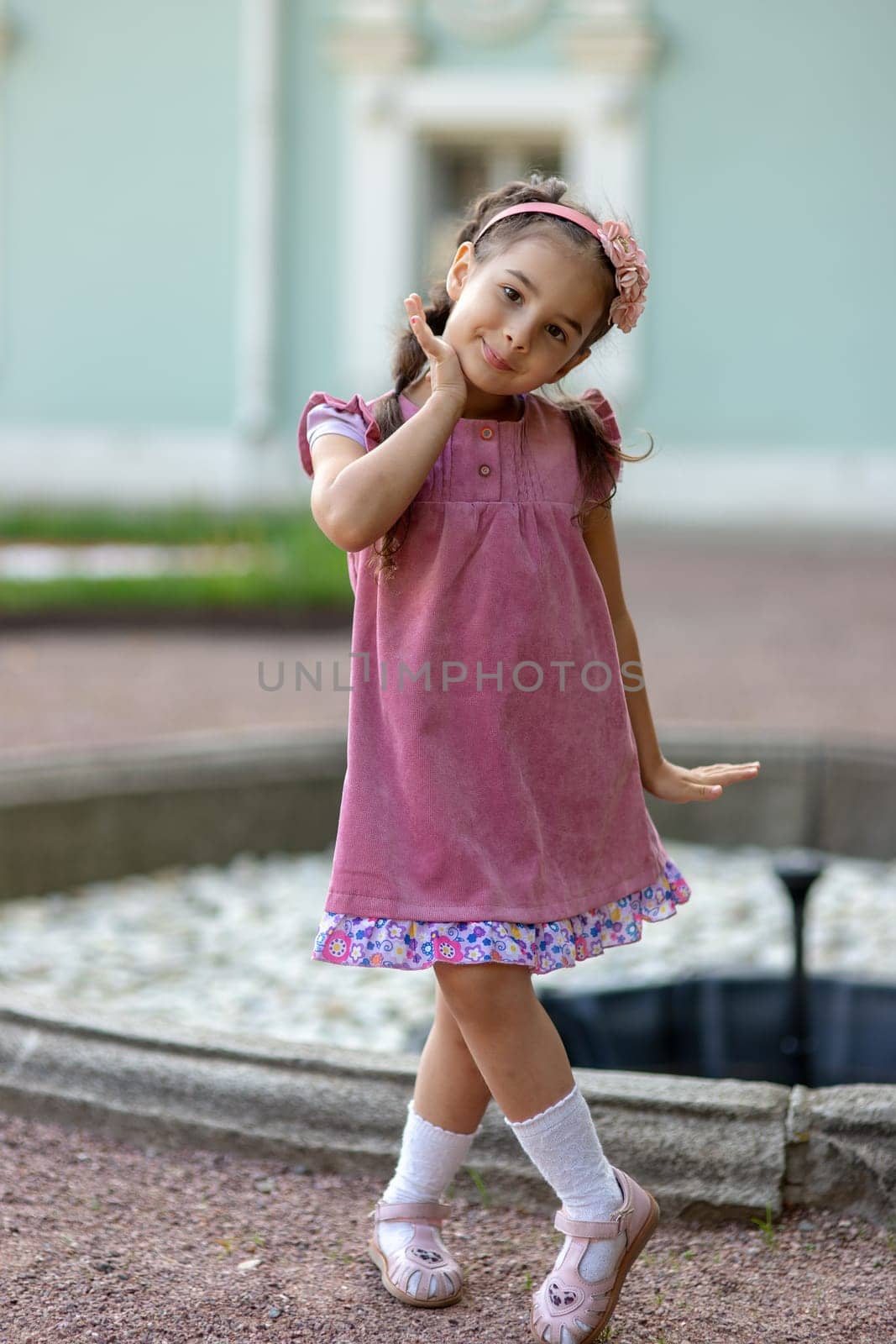 Young hispanic girl in pink dress posing outdoors by fountain.
