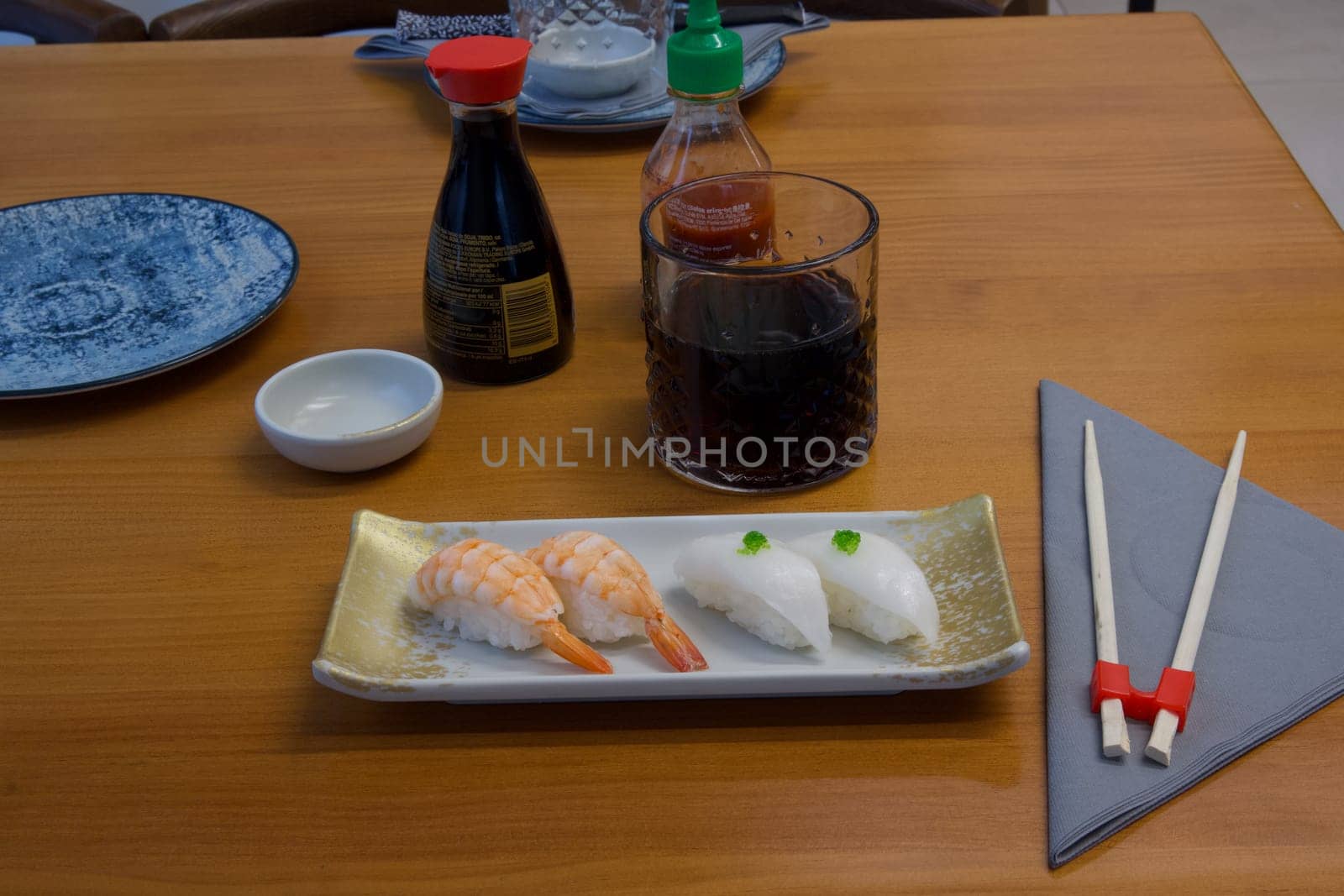 A plate of sushi with a glass of soda and chopsticks on a table. Scene is casual and relaxed, as it is a typical setting for enjoying a meal with friends or family