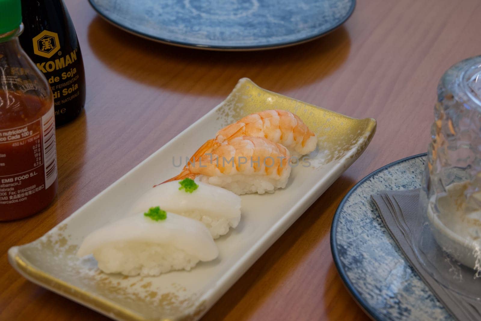 A plate of sushi with a bottle of soy sauce next to it. The sushi is arranged in a way that it looks like a small stack of three pieces