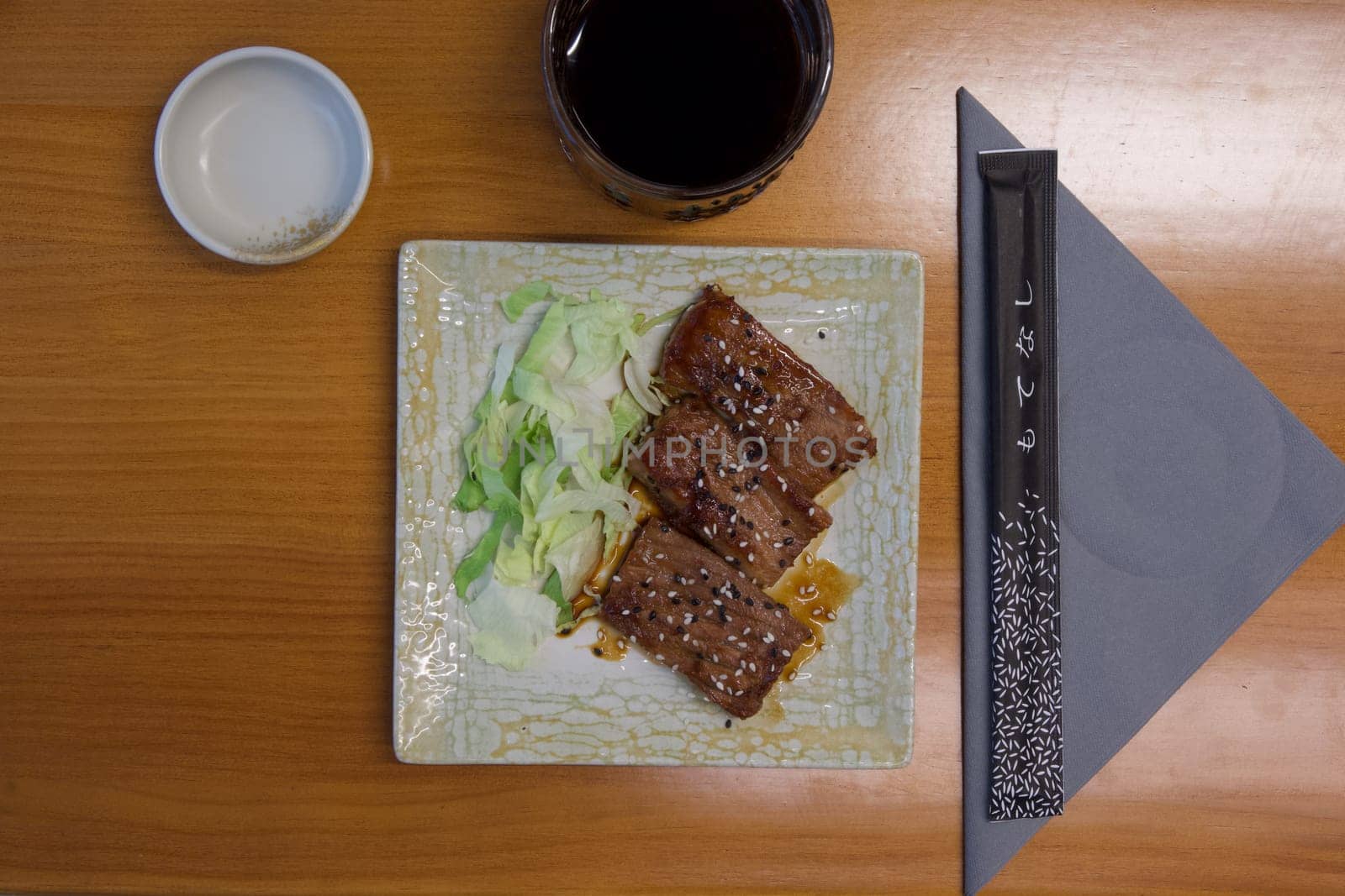 A plate of meat and vegetables sits on a wooden table. A cup of coffee is next to the plate
