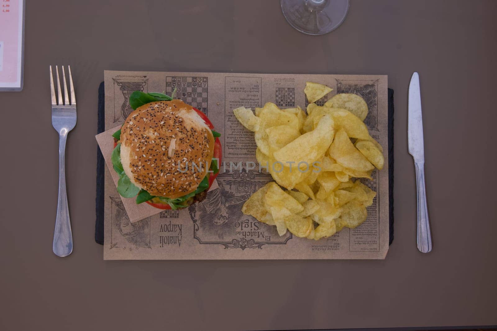 A plate of food with a burger and chips on top of a newspaper. Scene is casual and relaxed, as it is a simple meal with no fancy presentation