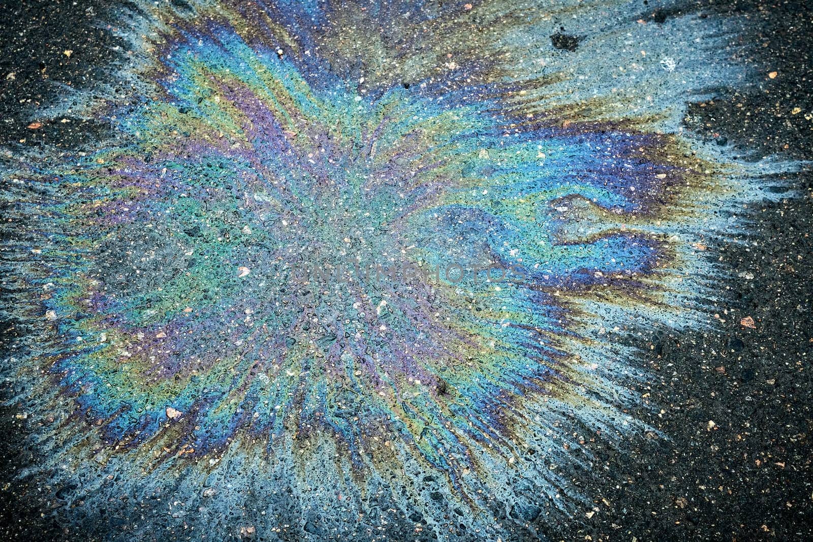 Colorful oil spill generating a vivid rainbow reflection on the dark pavement of the road