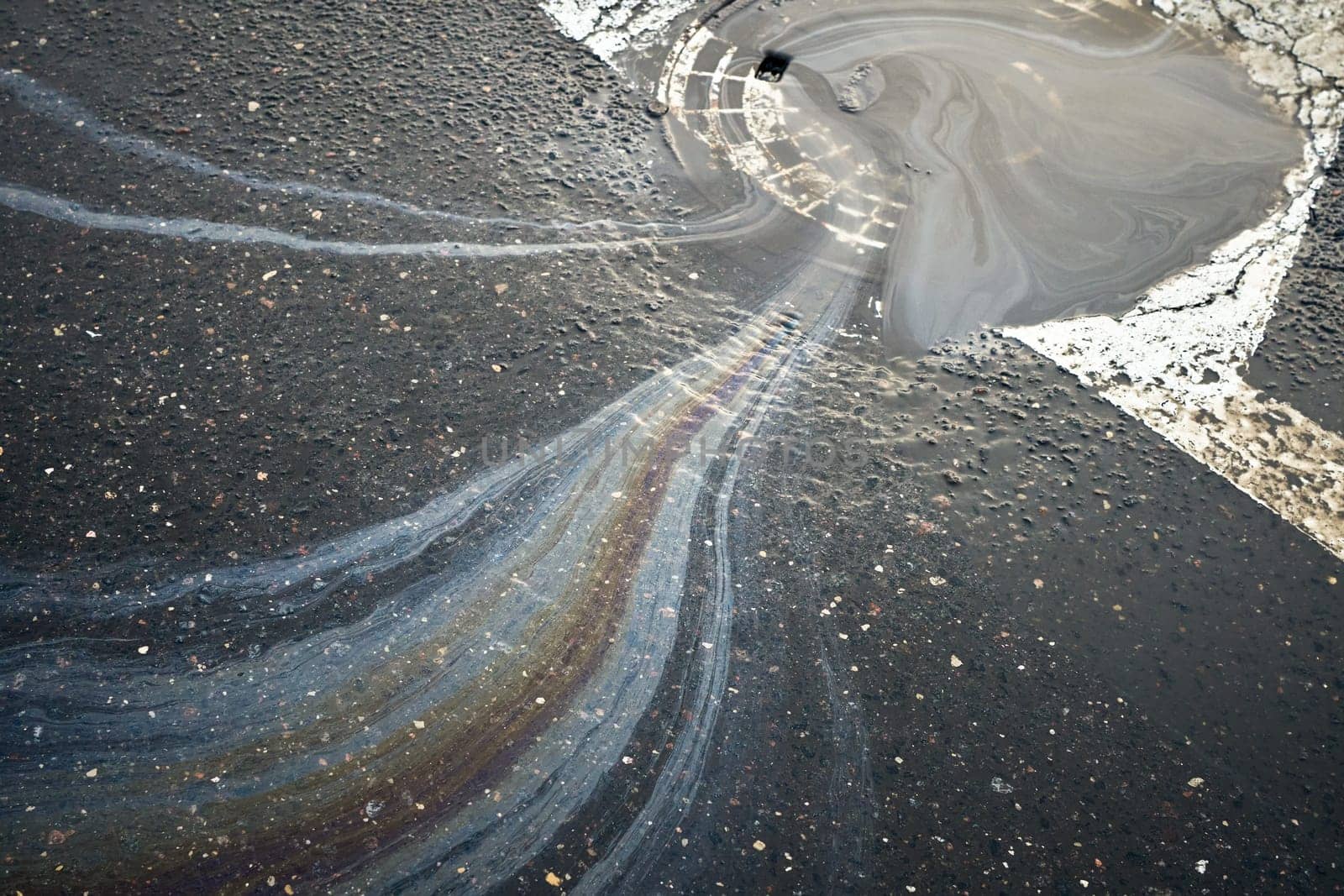 Colorful gasoline or oil spill polluting a wet asphalt road surface.