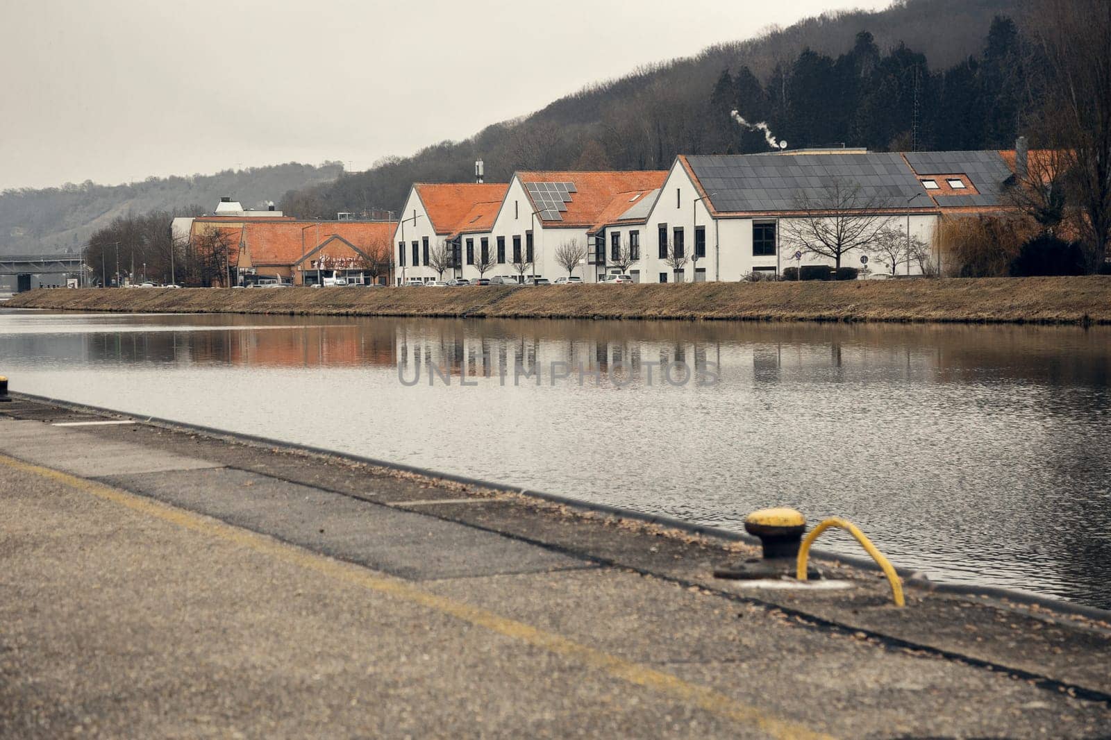 Modern white buildings with red-tiled roofs and solar panels on a riverbank. Their reflection in the calm water enhances the industrial yet serene atmosphere of the scene