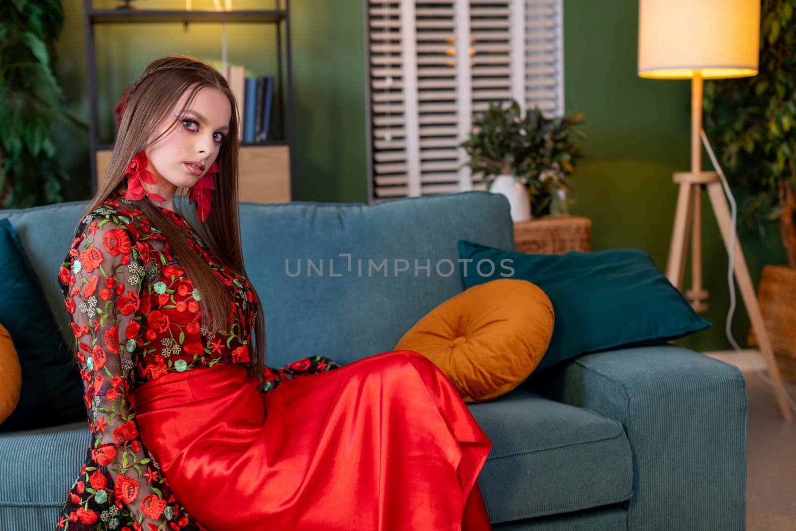 In a stylish and contemporary interior, a woman in a vibrant and eyecatching dress poses with gracefulness