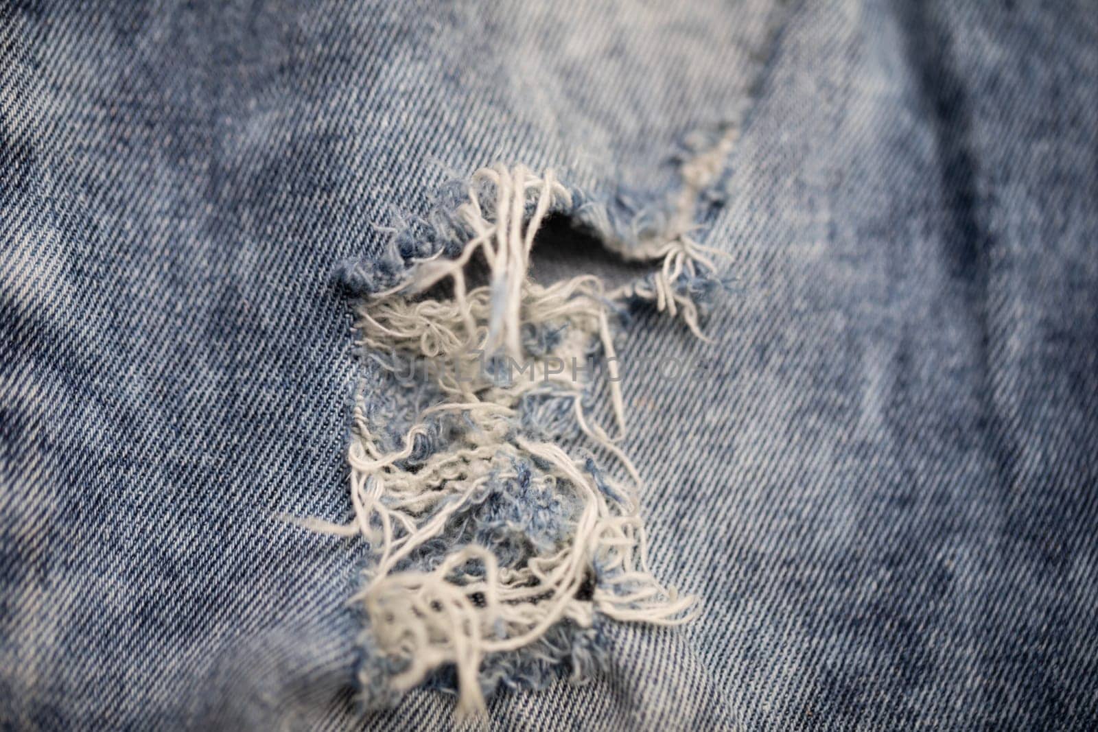 A closeup detailed view of a ripped denim fabric prominently showcasing its frayed edges and various blue tones