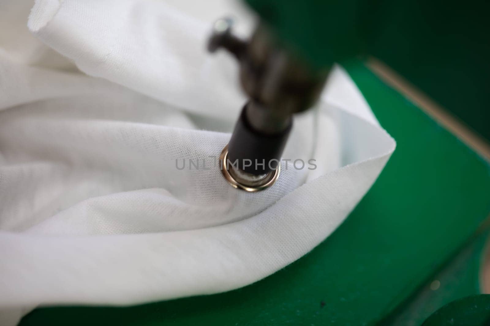 This is a closeup view of a specialized grommet machine that is setting a metal grommet into fabric material