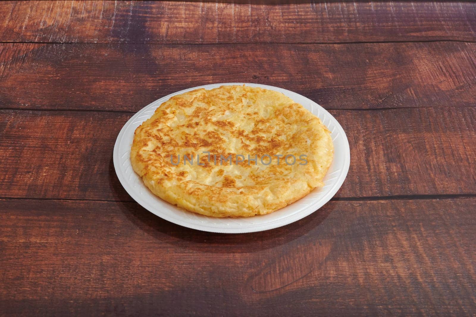 A plate of food with a yellowish brown crust sits on a wooden table. The plate is white and the food is round