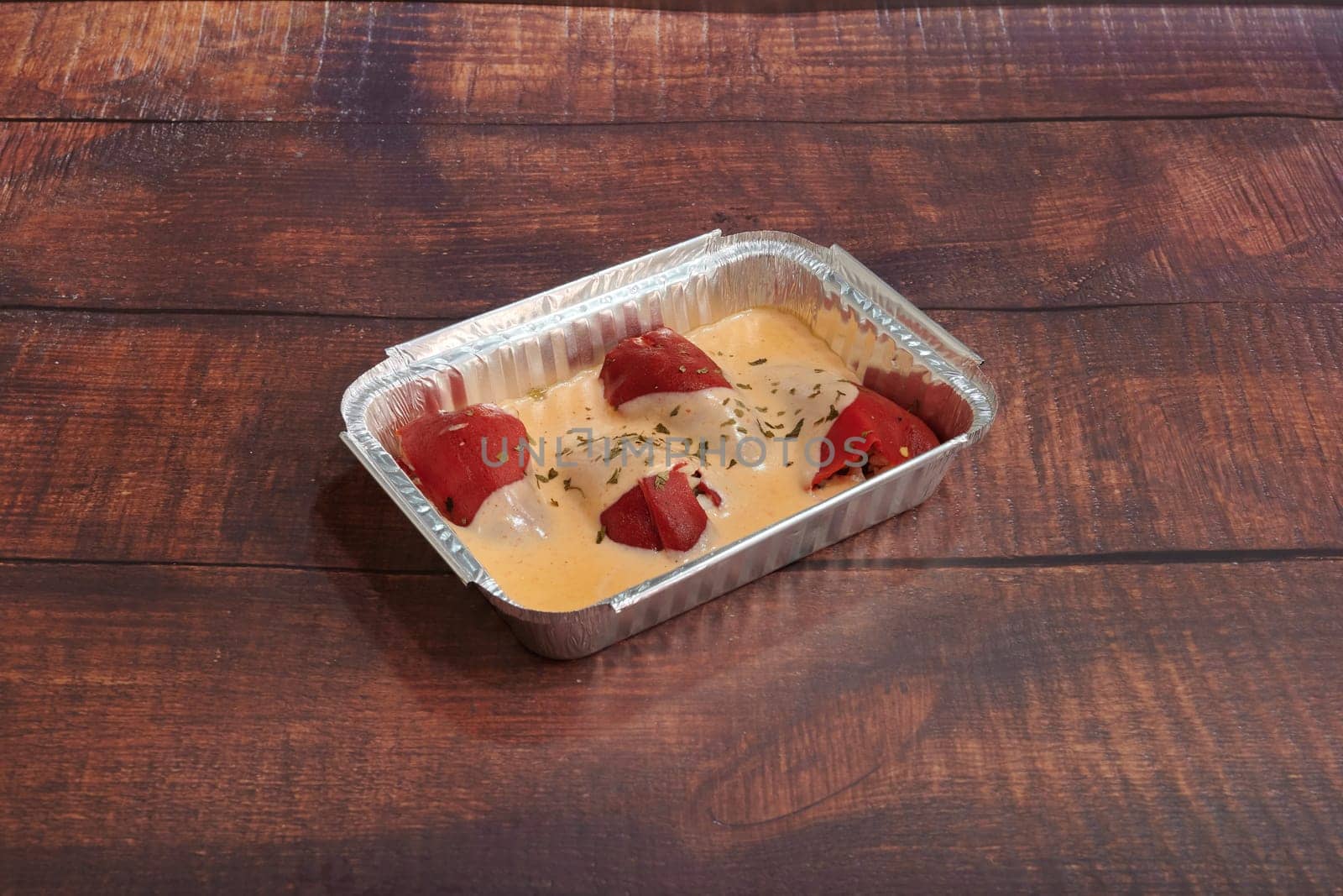 A small tray of food with a creamy sauce and red meat. The tray is on a wooden table