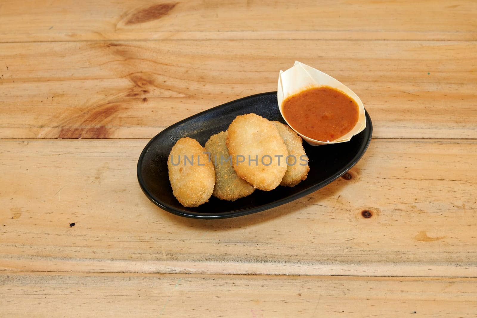 A plate of four fried food items with a sauce on the side. The plate is on a wooden table