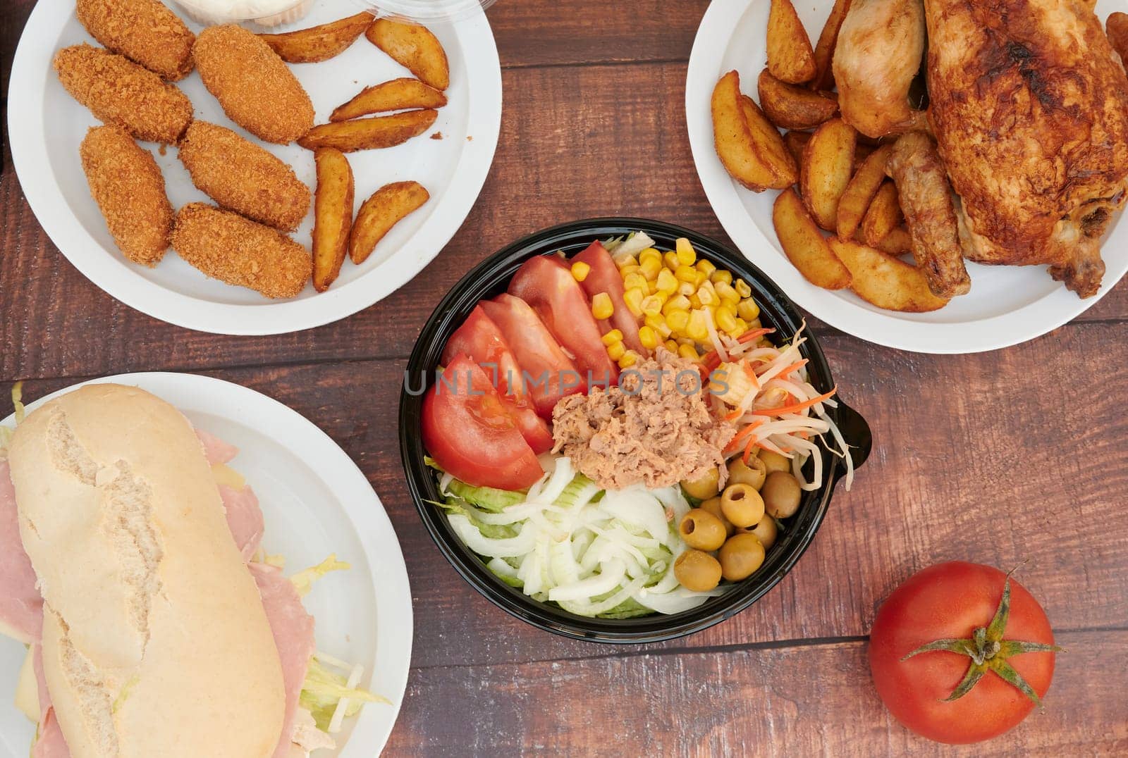 A variety of food is displayed on a table, including sandwiches, chicken, potatoes, and vegetables. The table is set for a meal, and the food looks delicious and inviting