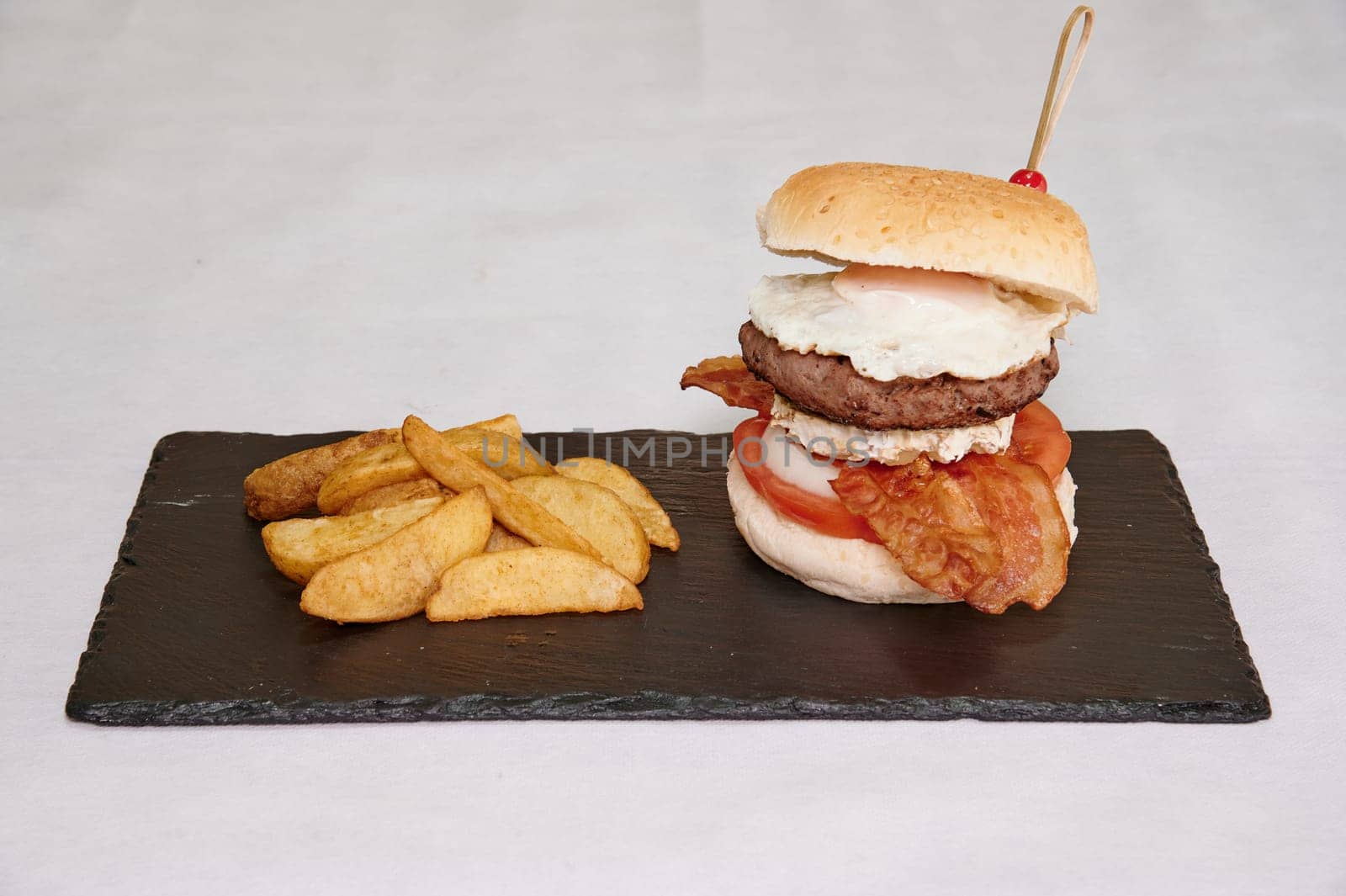 A burger with bacon and egg on top of a black plate. The burger is on a white background