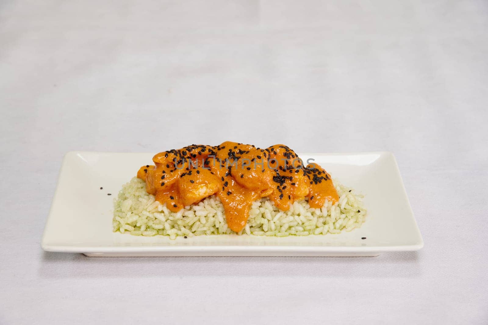 A plate of food with rice and chicken. The rice is brown and the chicken is orange. The plate is white and the food is on a white table