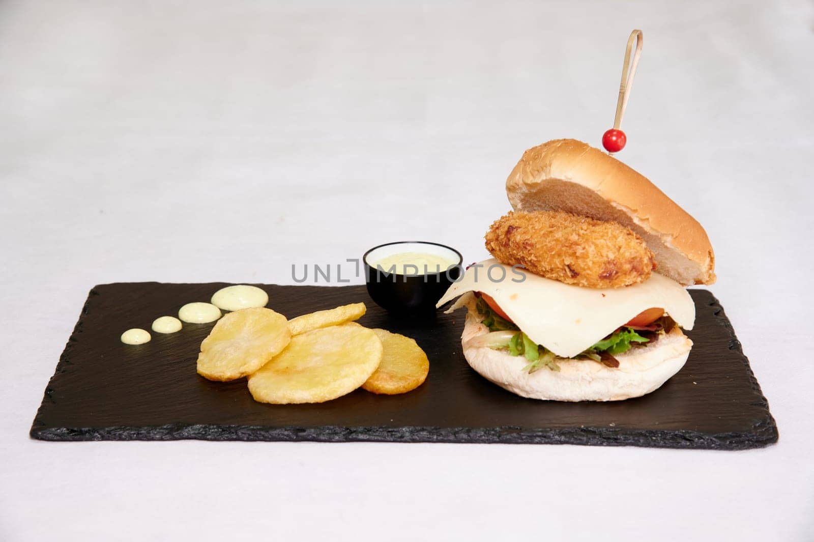 A sandwich with a bun and a piece of meat on top of it. The sandwich is served on a black plate with a side of fries