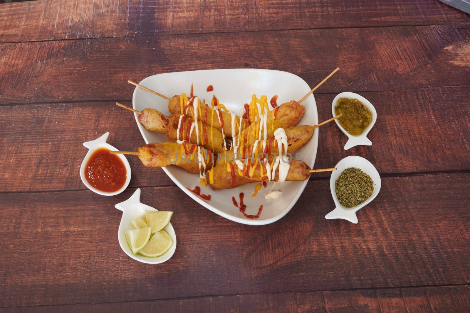 A plate of food with a variety of condiments and a few skewers of food. Scene is casual and inviting, as it is a meal shared among friends or family