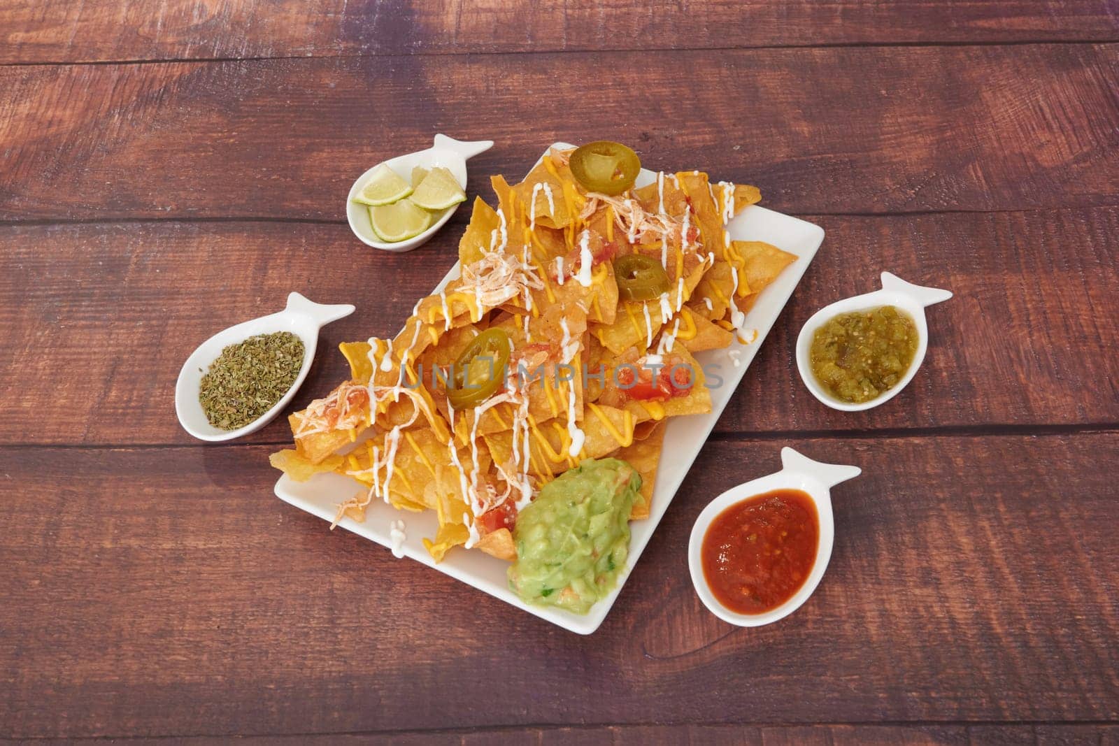A plate of nachos with a variety of sauces and toppings. The plate is set on a wooden table