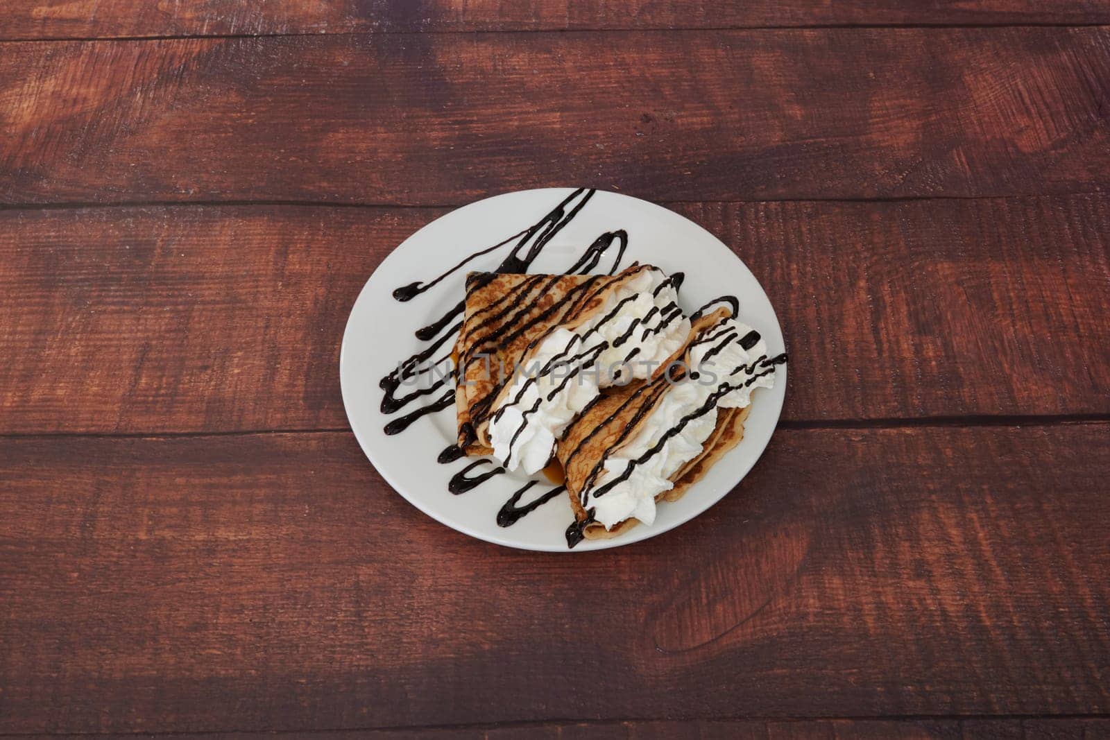 A dessert with chocolate sauce and whipped cream is placed on a white plate. The dessert is a delicious treat that is perfect for satisfying one's sweet tooth. The chocolate sauce adds a rich