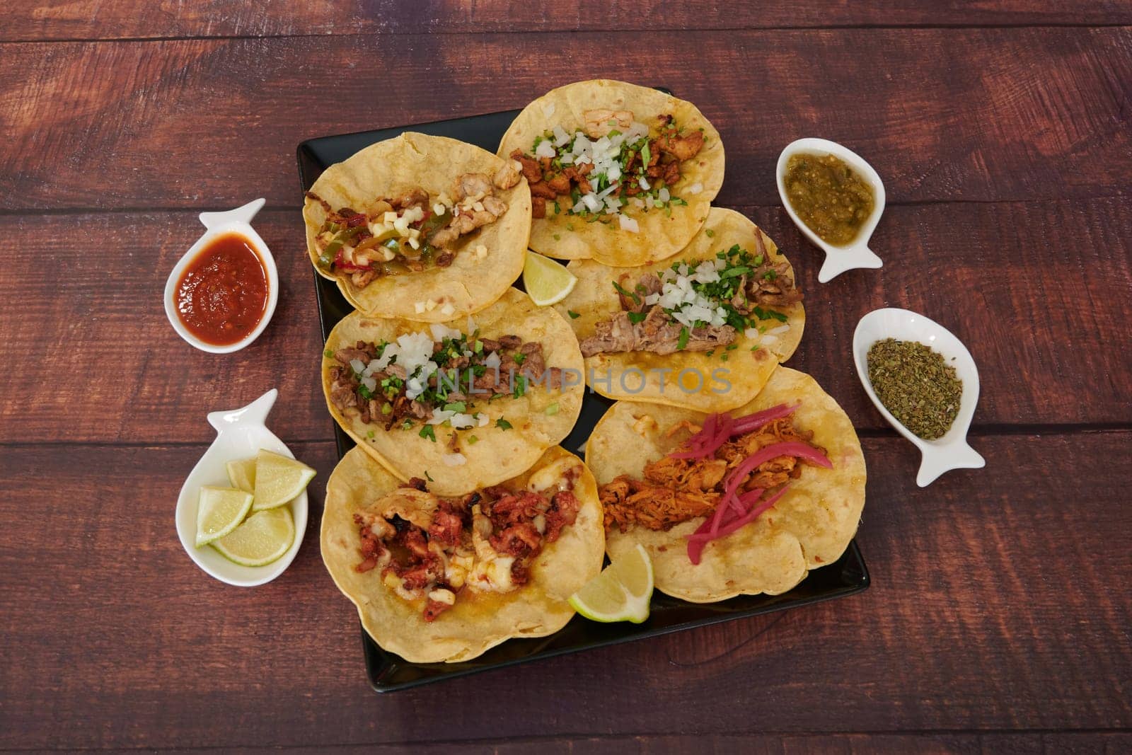 A plate of Mexican food with a variety of tacos and a bowl of salsa. Concept of abundance and variety, as there are at least nine different types of tacos on the plate