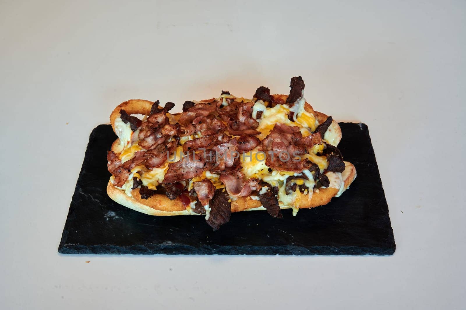 A bacon and cheese sandwich is on a black table. The sandwich is large and has a lot of bacon and cheese