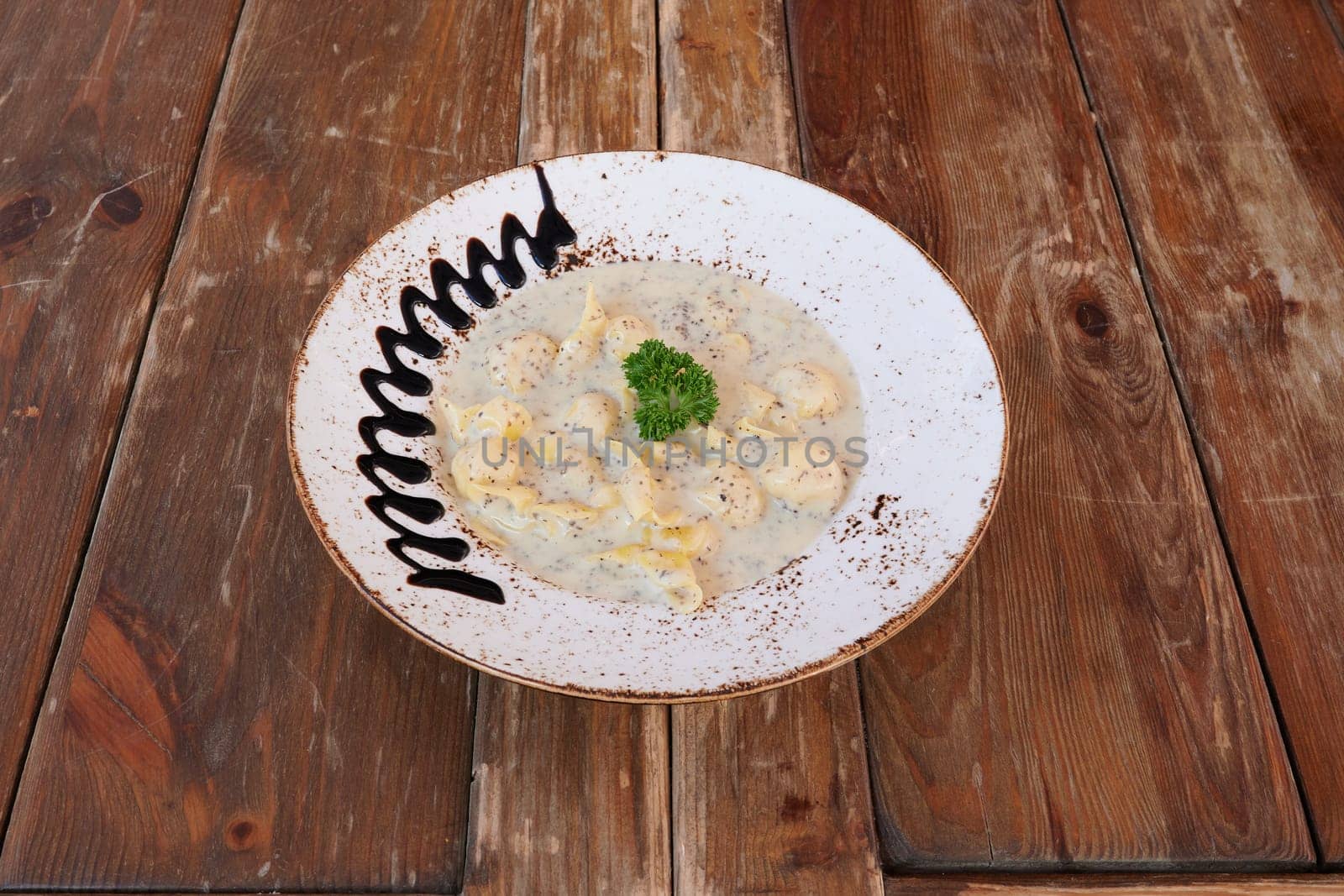 A bowl of pasta with parsley on top. The bowl is white and has a brown border