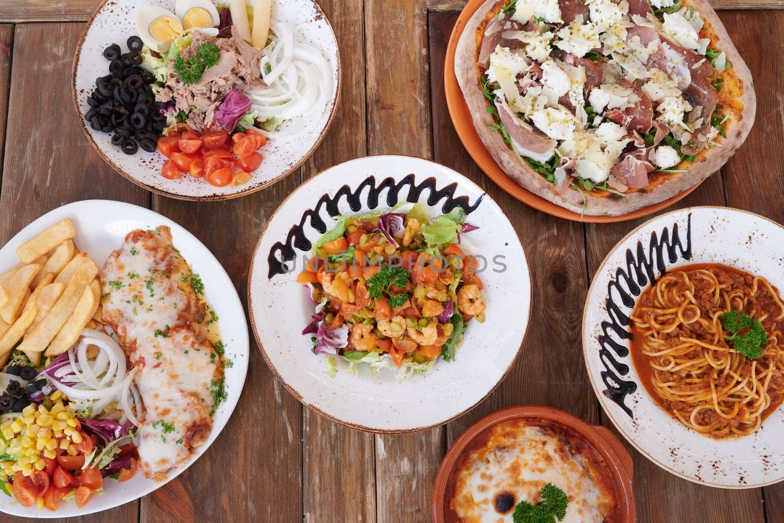 A table with a variety of food, including pizza, pasta, and salad. The table is set with plates and bowls, and the food is arranged in a visually appealing manner. Scene is inviting and appetizing