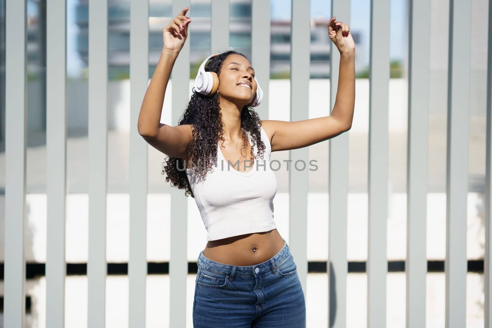 A very cheerful and lively young woman dances energetically while wearing fashionable headphones and a casual outfit, radiating pure joy and happiness against a vibrant and modern urban backdrop