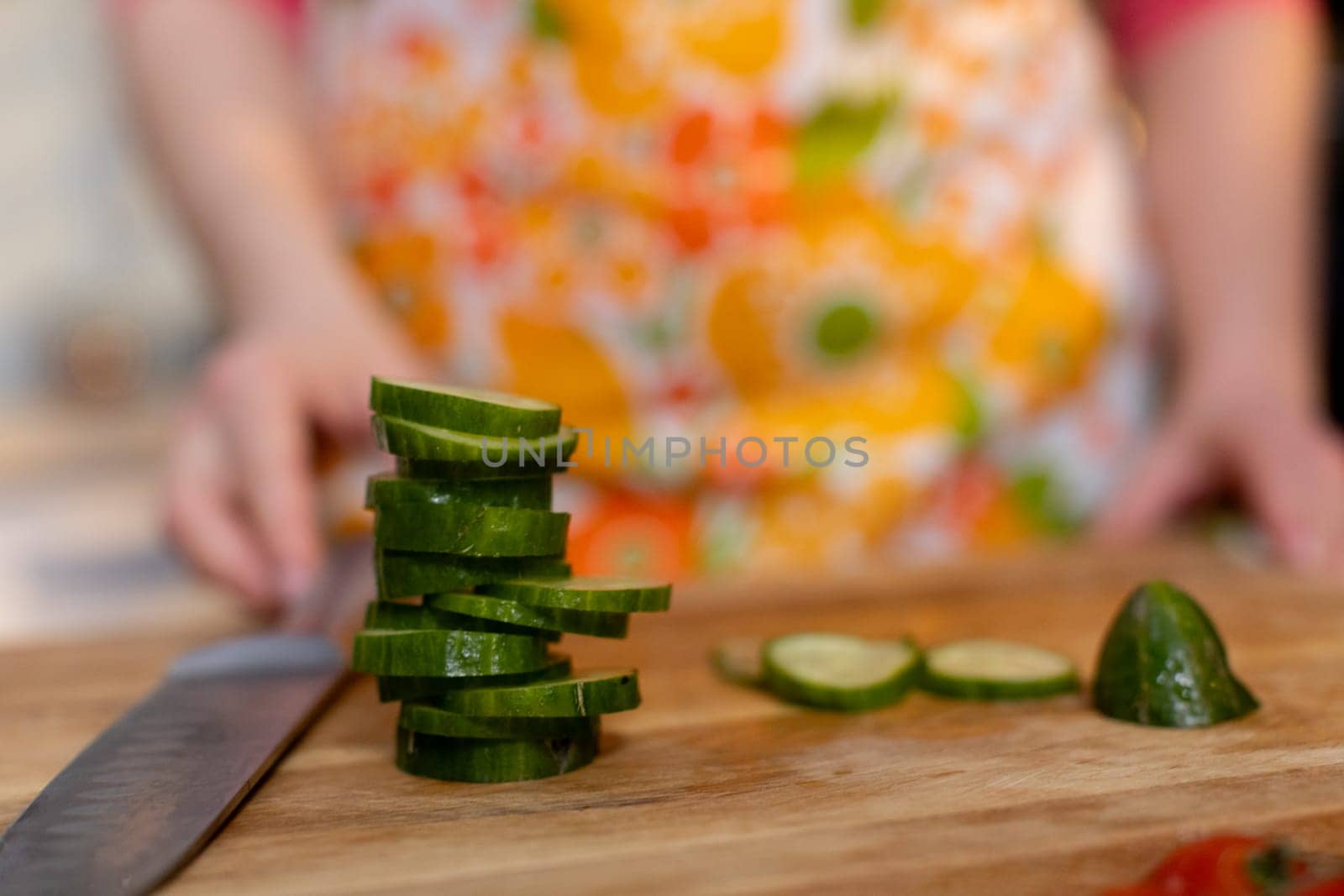 A vibrant scene of cucumbers being sliced on a wooden board with a colorful apron in the background.