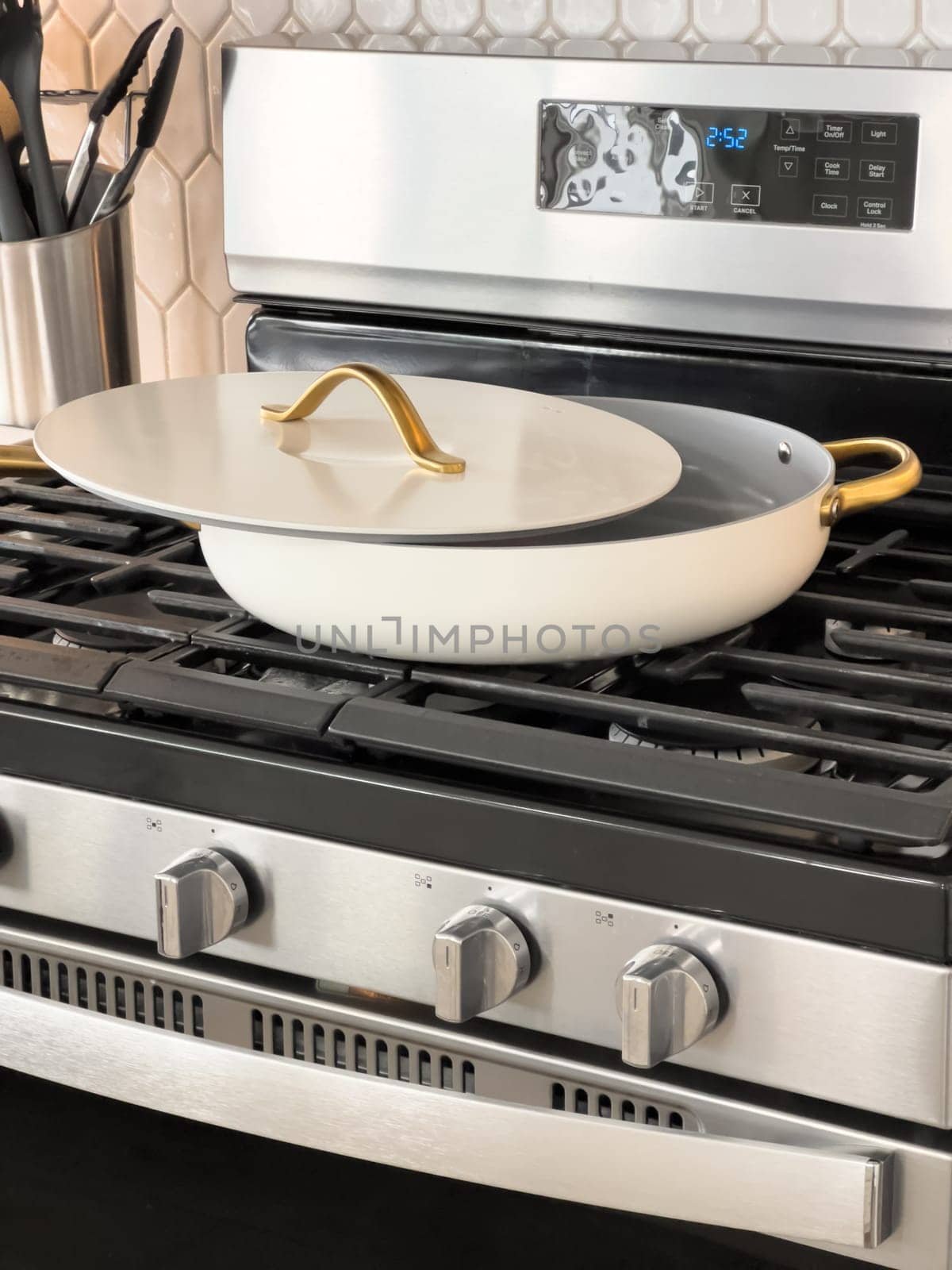 Castle Rock, Colorado, USA-January 18, 2025-A white cooking pan with gold handles and a matching lid sits on a gas stove The pan has a sleek modern design with a nonstick surface The stainless steel stove has multiple burners and a digital display The kitchen counter features a marble design with various cooking utensils in the background