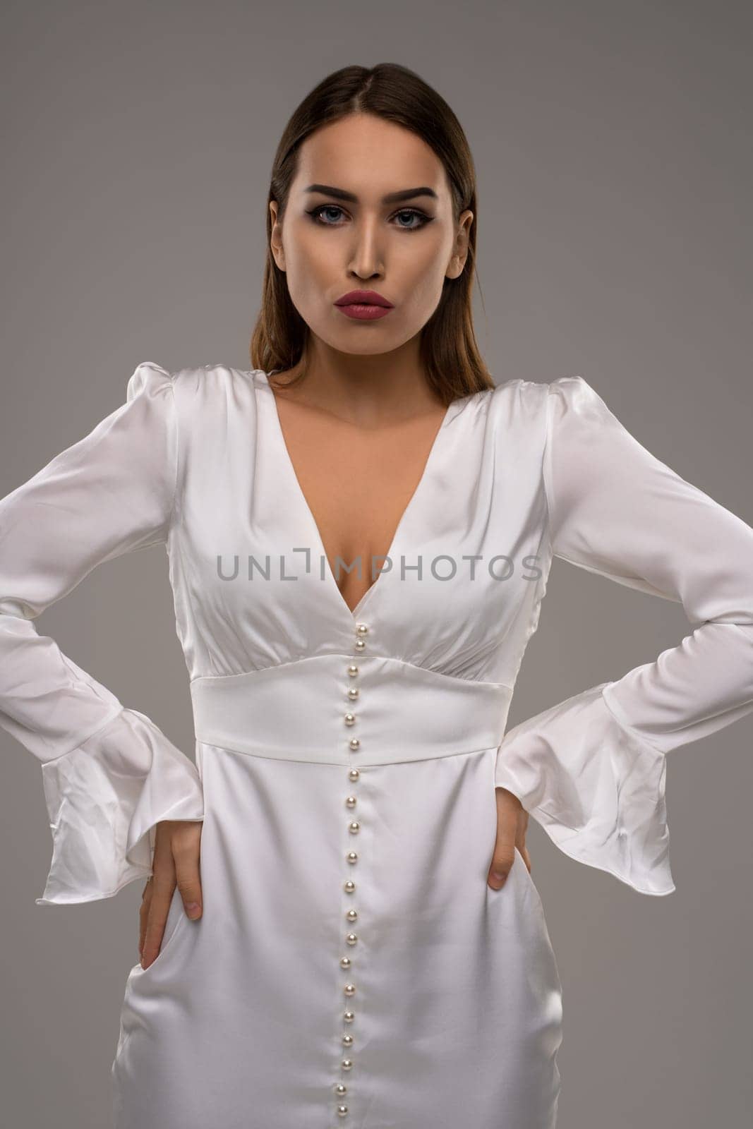Confident female model wearing white shiny dress looking at camera studio portrait