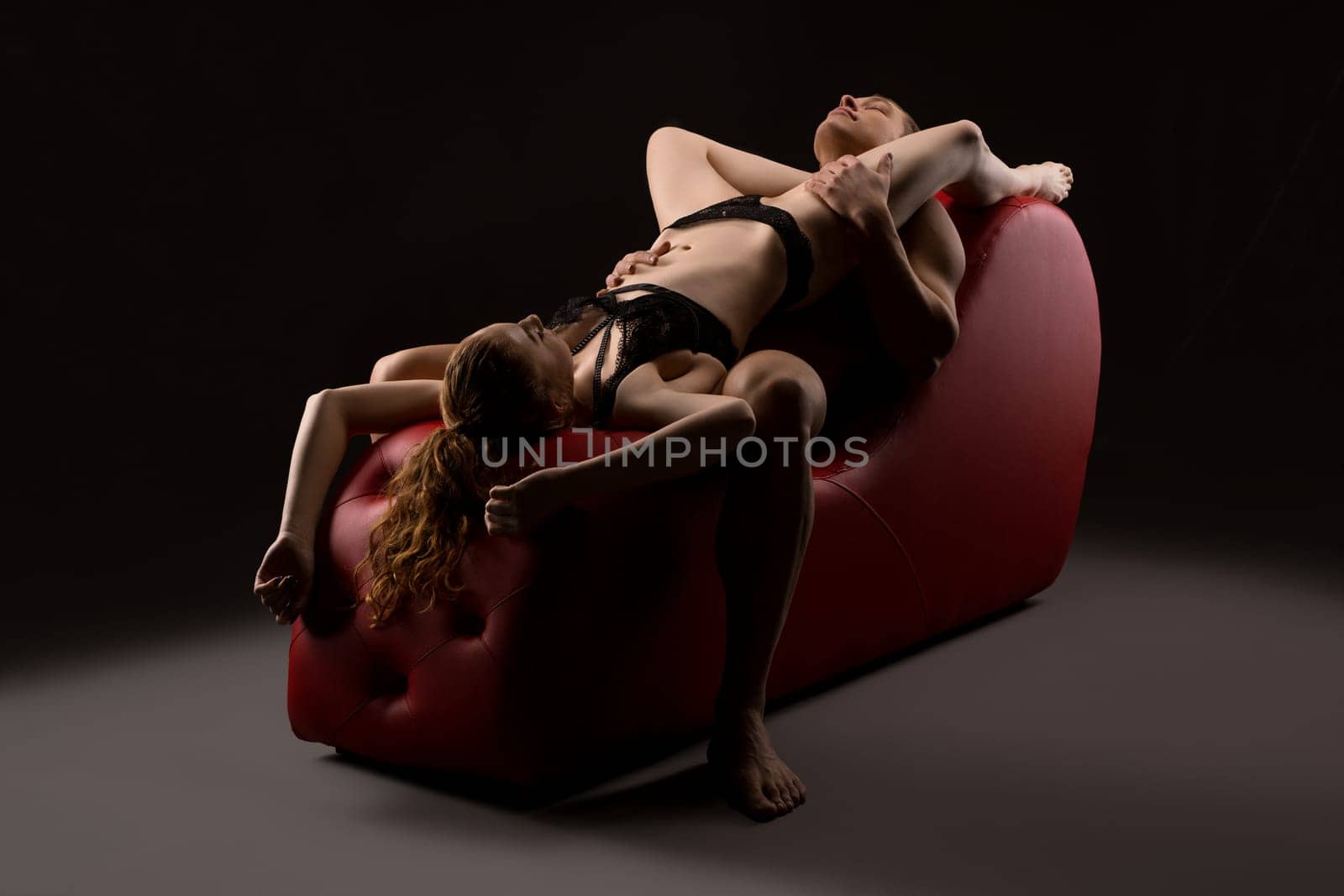 Sensual sexy couple enjoying intimate moments together on red leather chair in dark studio