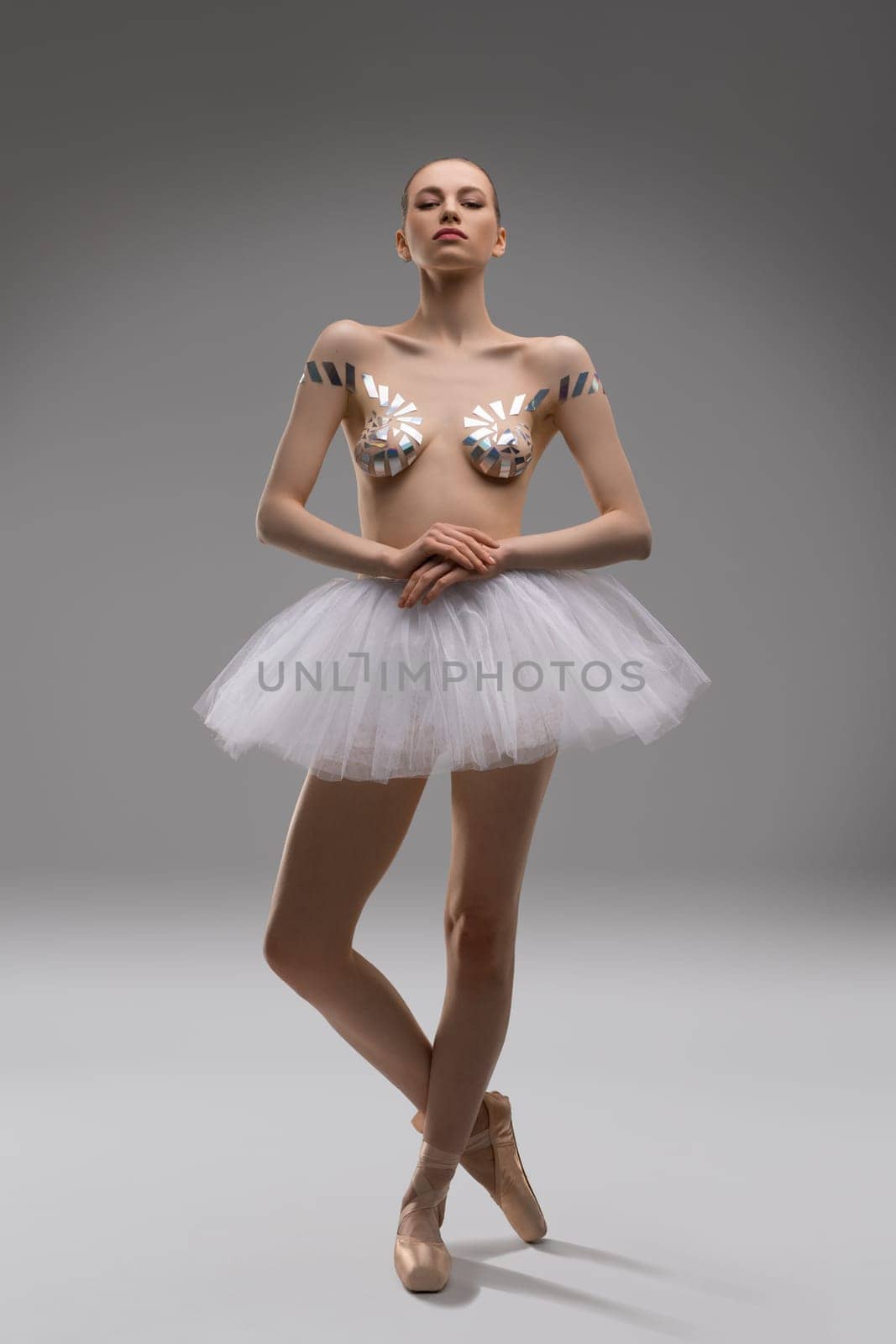 Attractive young slim female in ballet tutu skirt and with sticky tapes on breast posing in studio look at camera