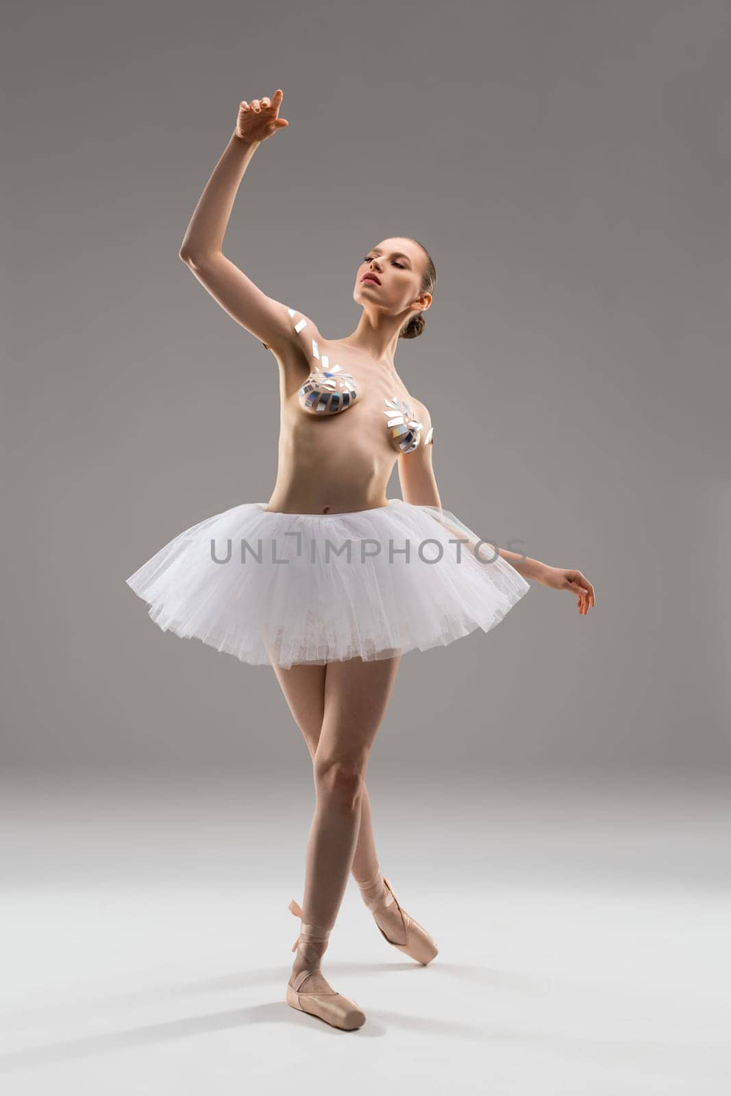 Attractive young slim female in ballet tutu skirt and with sticky tapes on breast posing in studio
