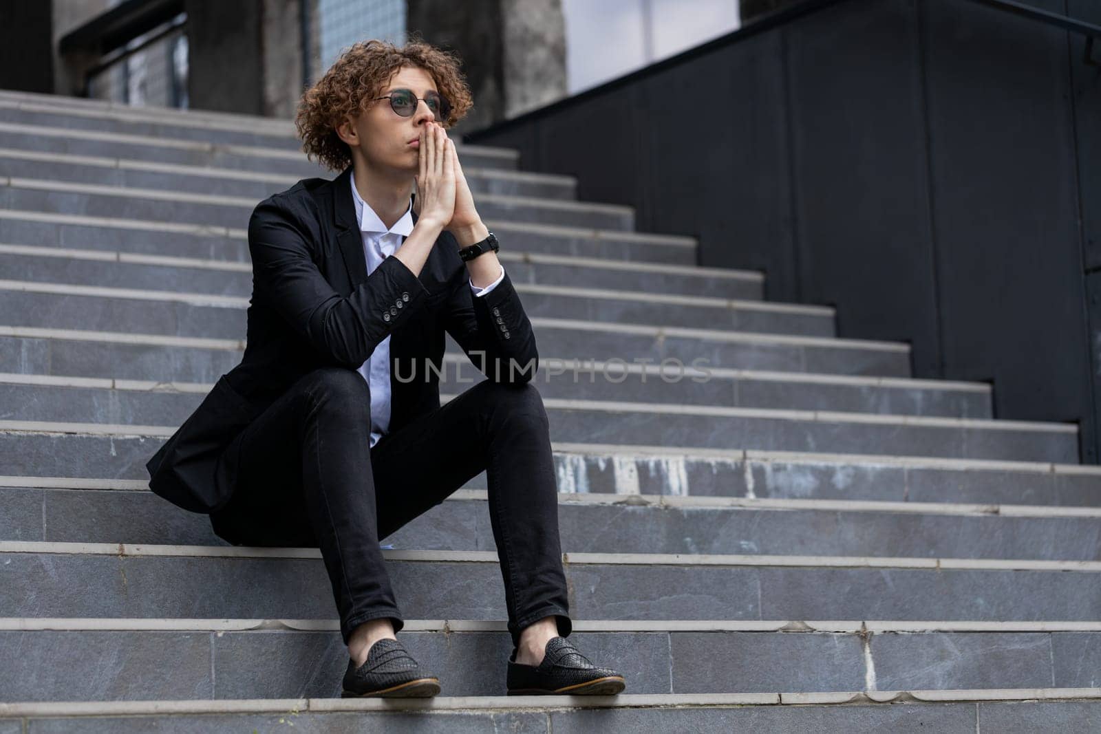 Nervous manager sitting on office steps. Pensive businessman in suit with hands joined making company decision. Successful CEO expert thinking silent break. Corporate leader pondering in downtown.